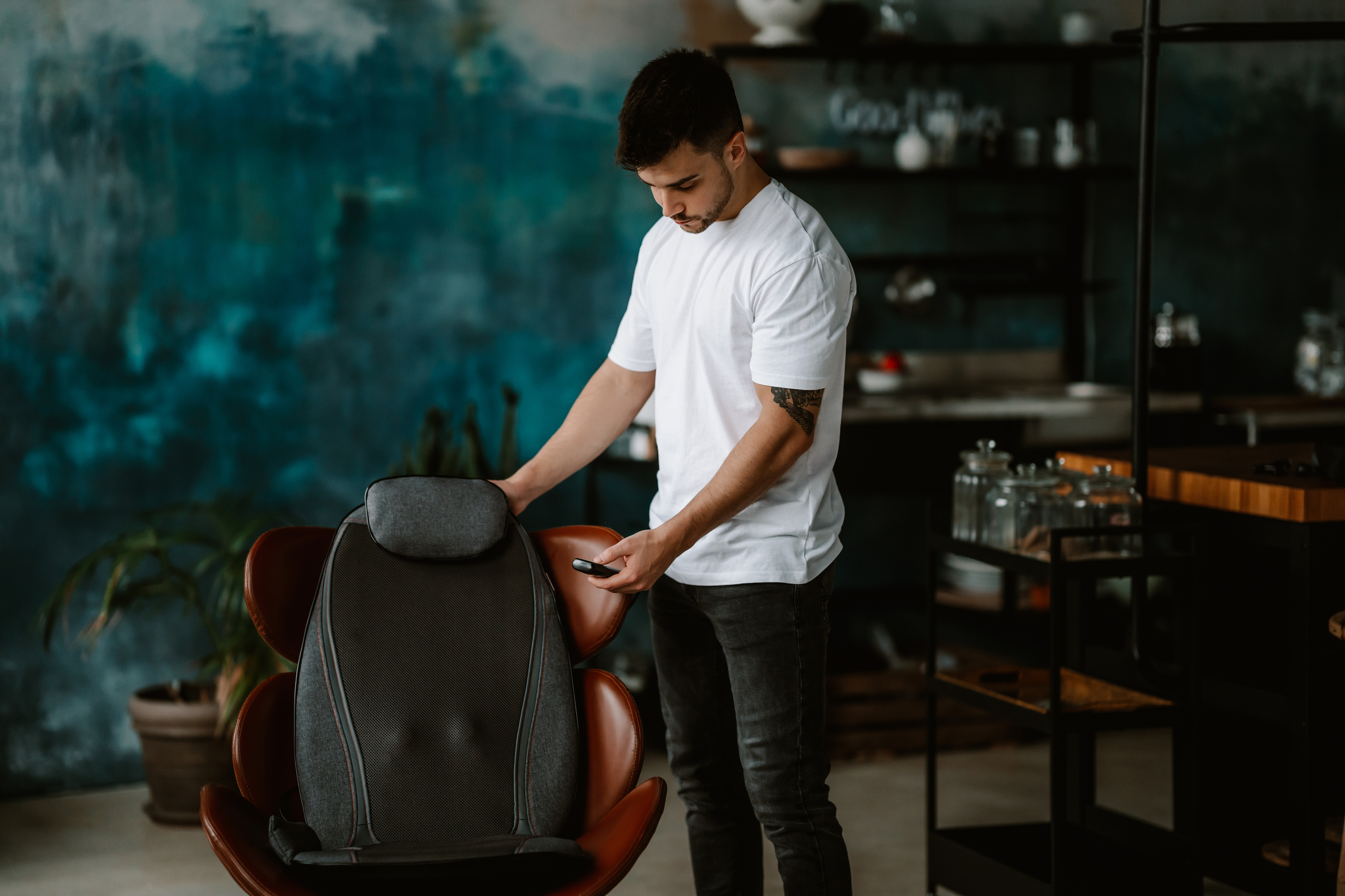 Mann, weißes Hemd, nutzt Handy, sitzt in der Nähe eines Massagesitzes.