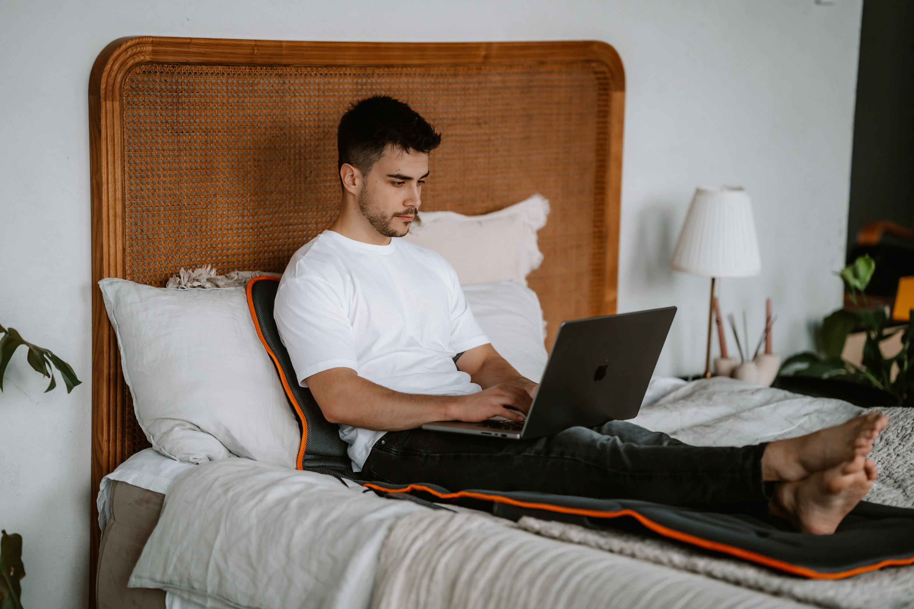 Mann im weißen Hemd, der einen Laptop benutzt, während er im Bett liegt.