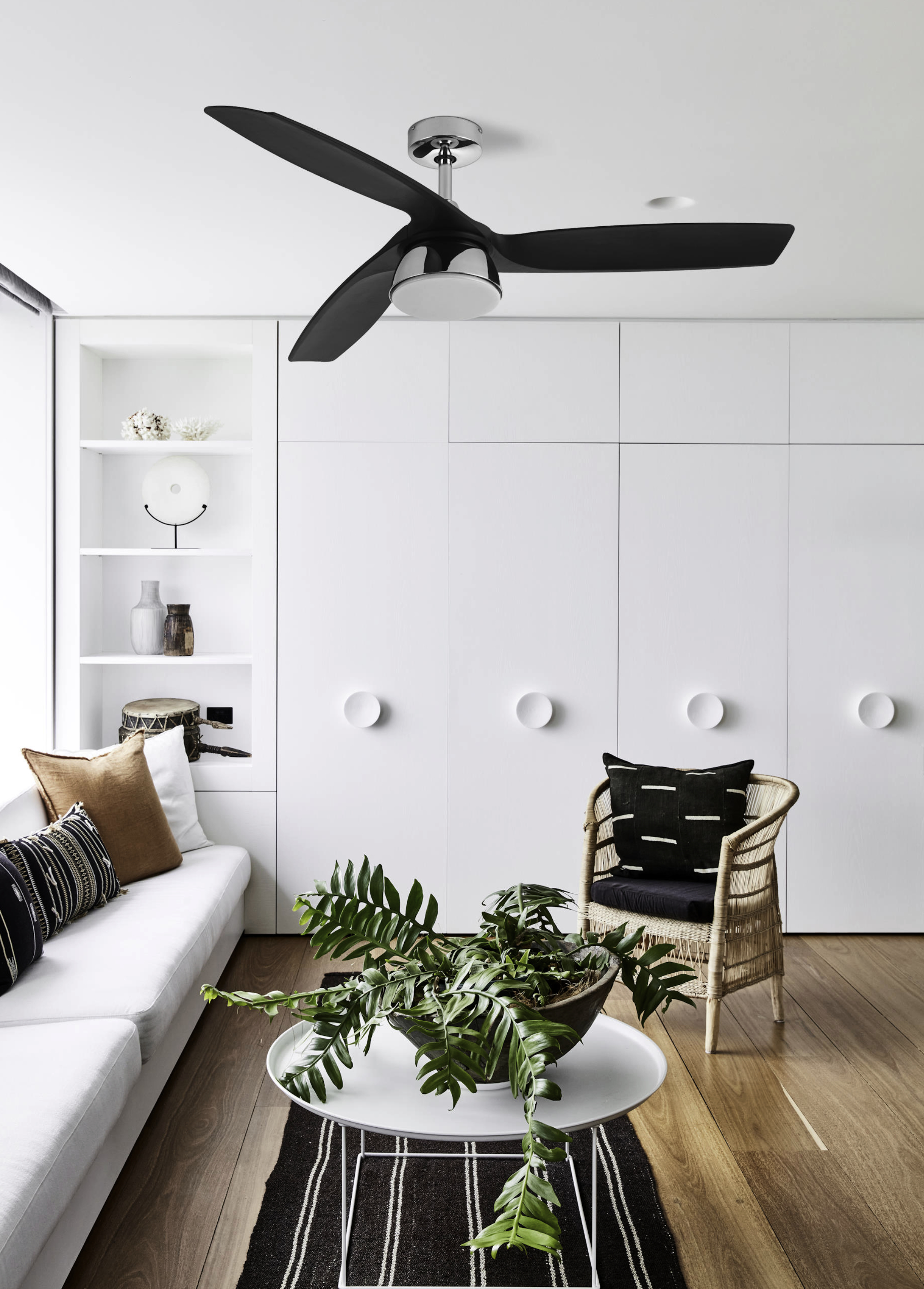 Wohnzimmer mit weißen Wänden, Deckenventilator und Sofa. Tisch und Pflanze sichtbar.