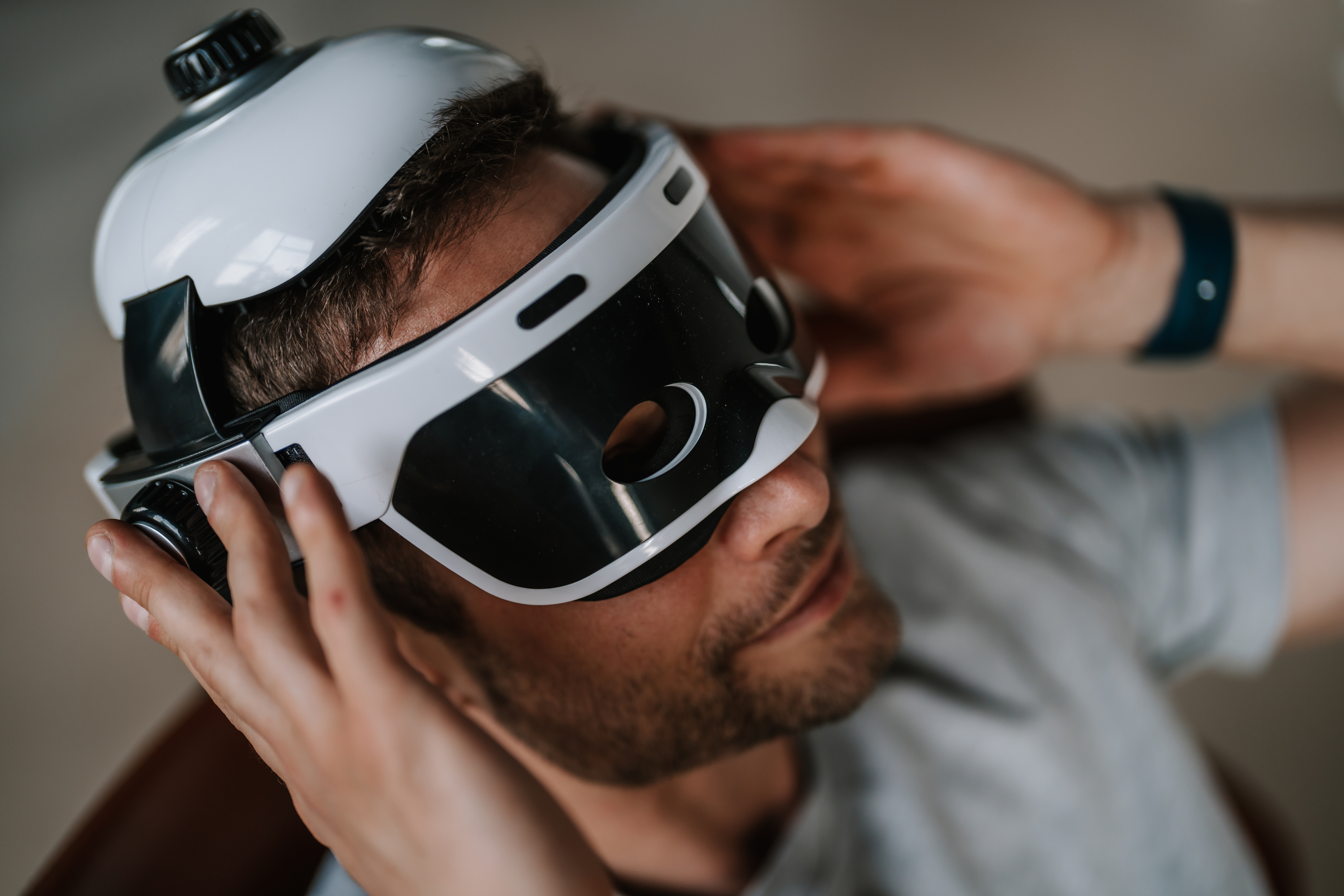 Mann trägt VR-Headset, Hände passen es an. Weißes und schwarzes Headset, Nahaufnahme.