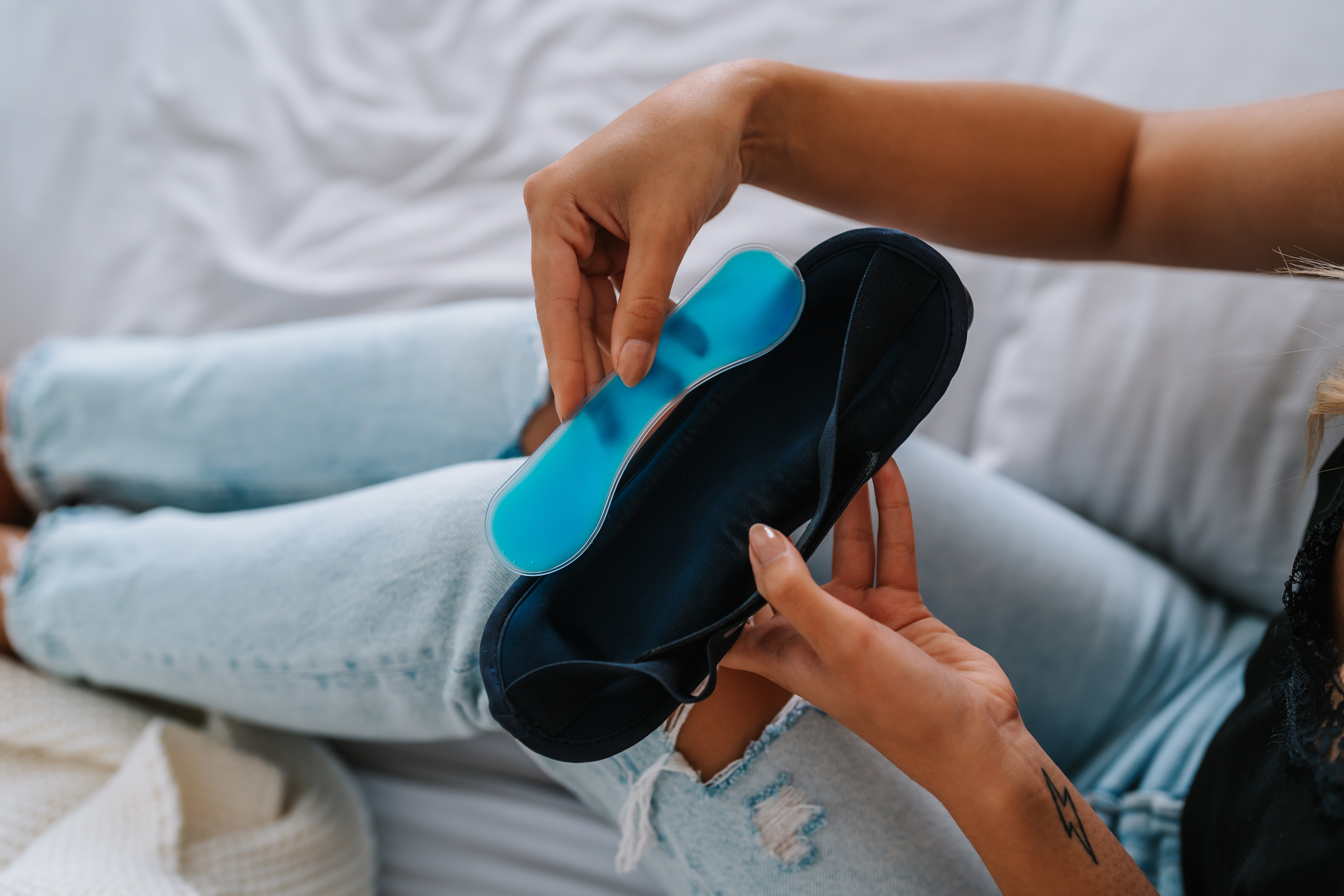 Hände einer Person halten eine blaue Einlegesohle neben einem schwarzen Schuh auf einem Bett.