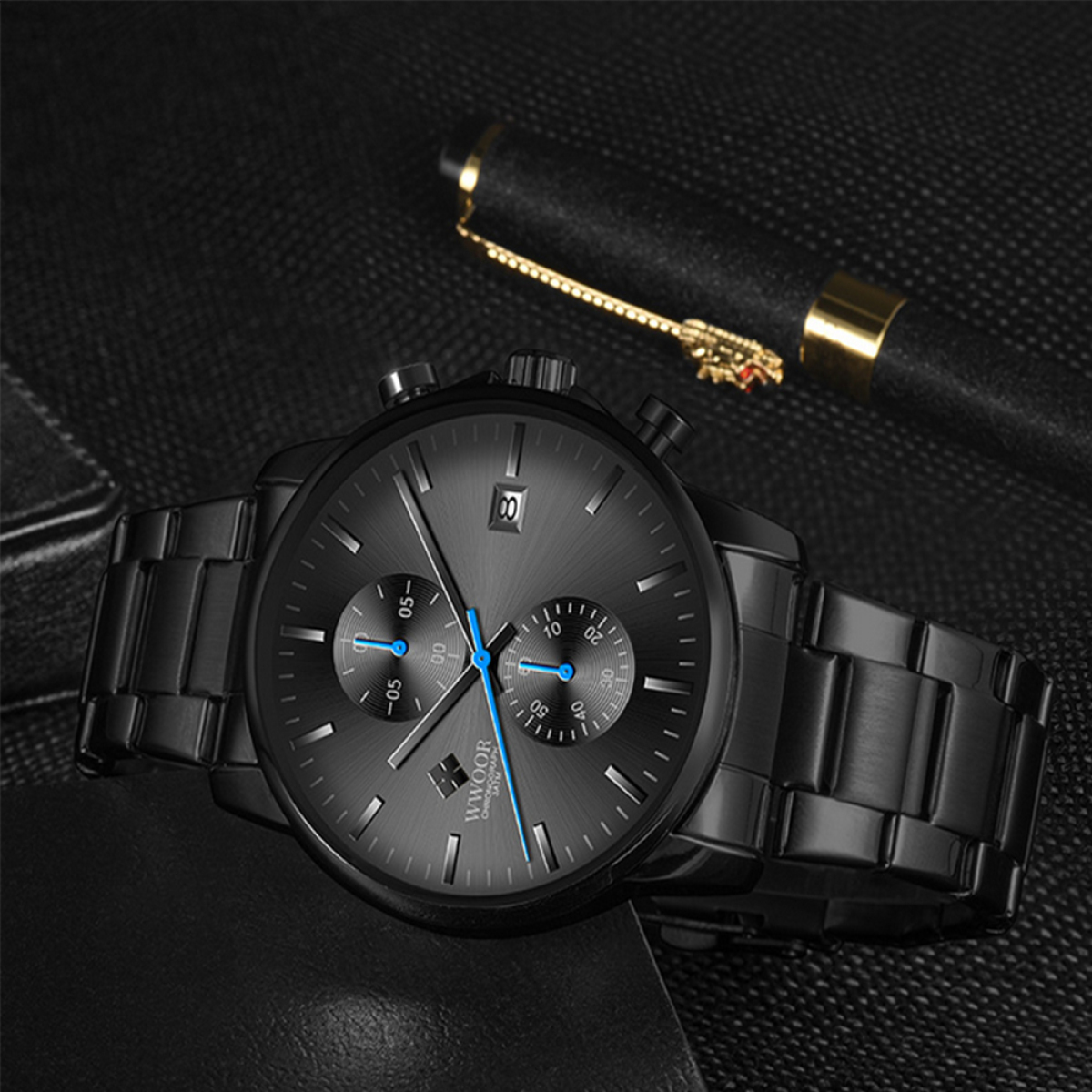 Schwarze Uhr mit schwarzem Armband, silbernem Zifferblatt und Stift im Hintergrund.