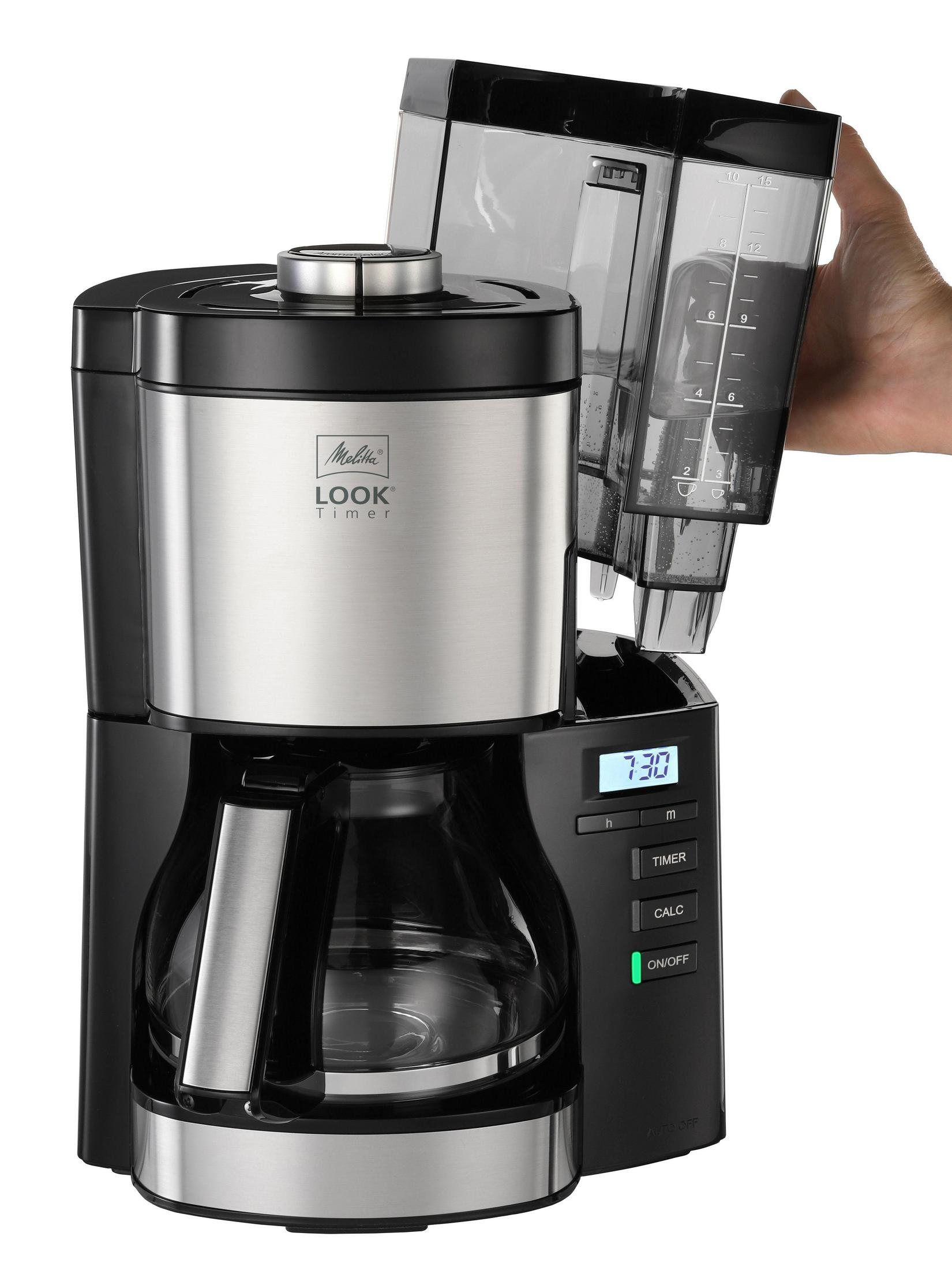 Czarno-srebrny ekspres do kawy. Dłoń trzyma pojemnik na wodę z oznaczeniami.