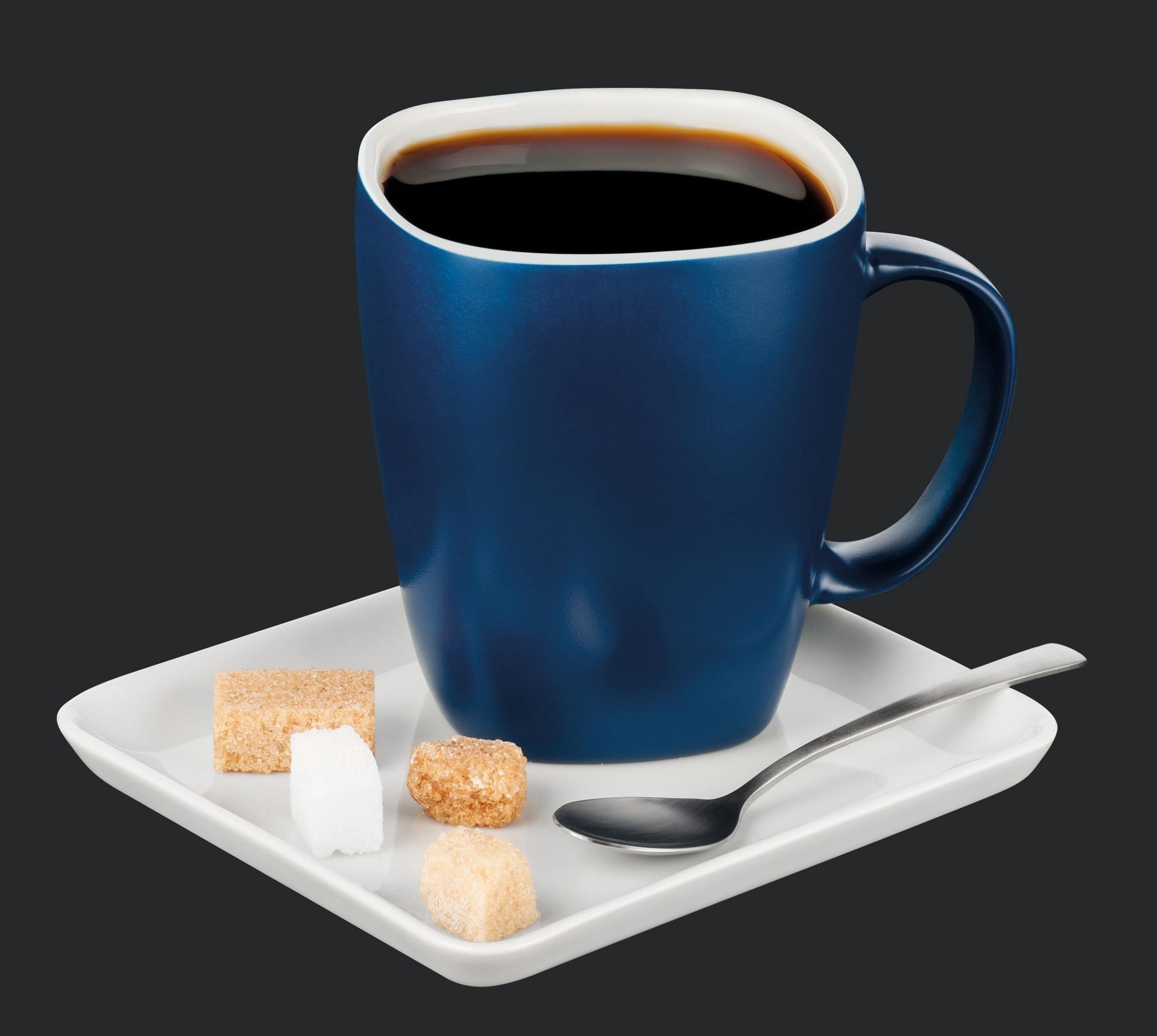 Eine blaue Tasse mit schwarzem Kaffee, ein weißer Teller mit Würfelzucker und ein Löffel auf dunklem grauem Hintergrund.