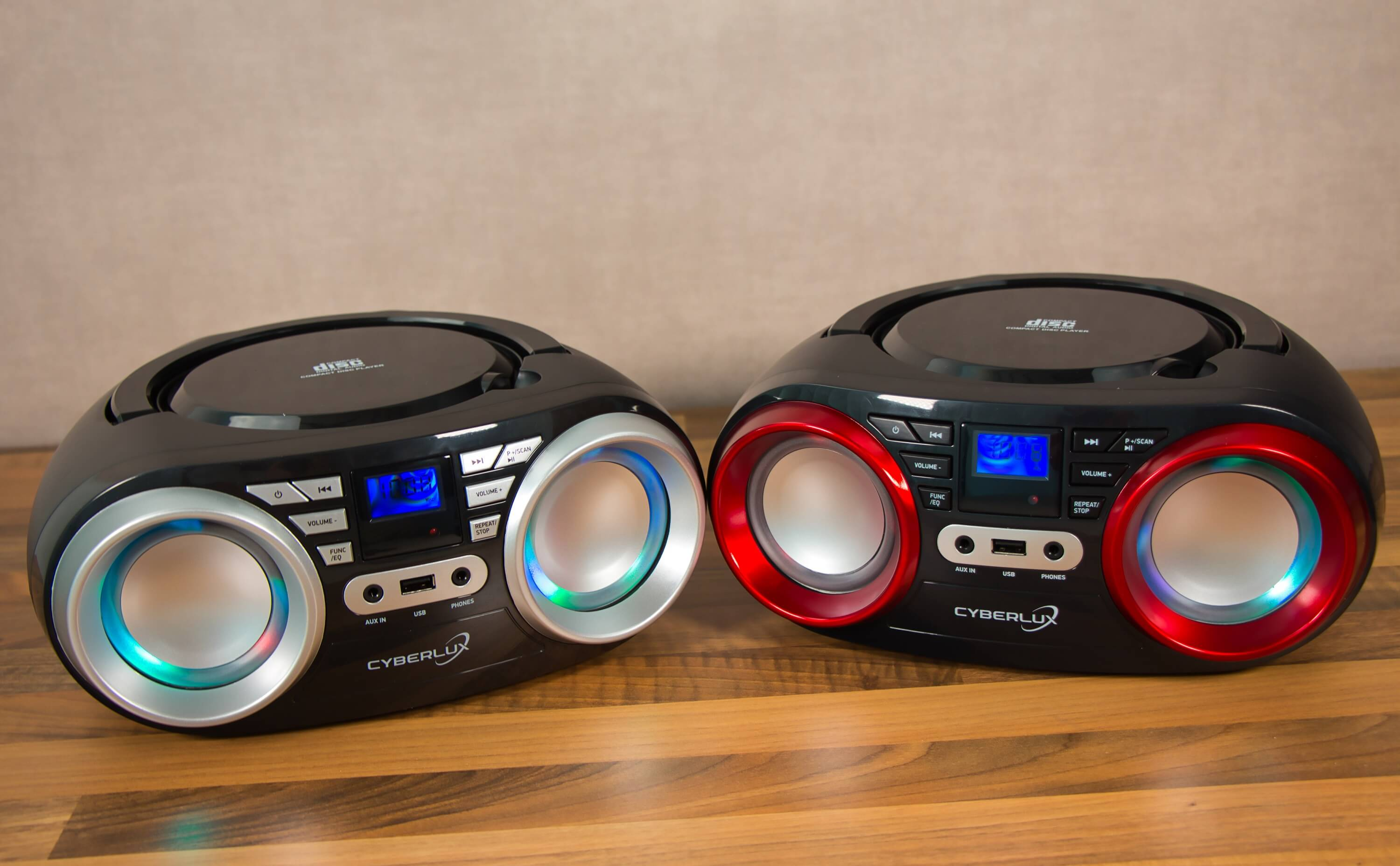 Zwei schwarze CD-Player mit silbernen Lautsprechern und blauer Beleuchtung auf Holzoberfläche.