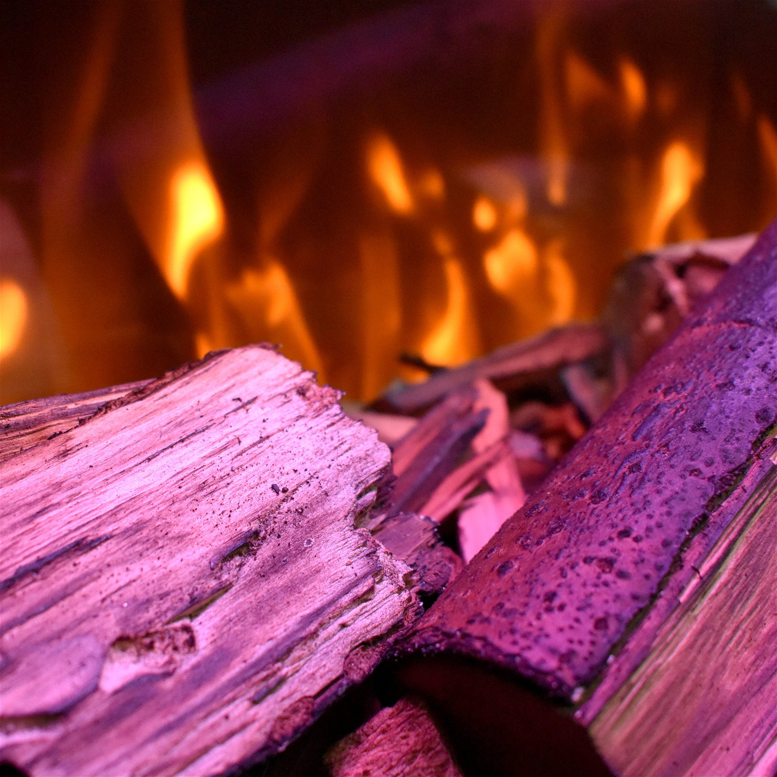 Nahaufnahme von brennendem Brennholz mit Flammen im Hintergrund.