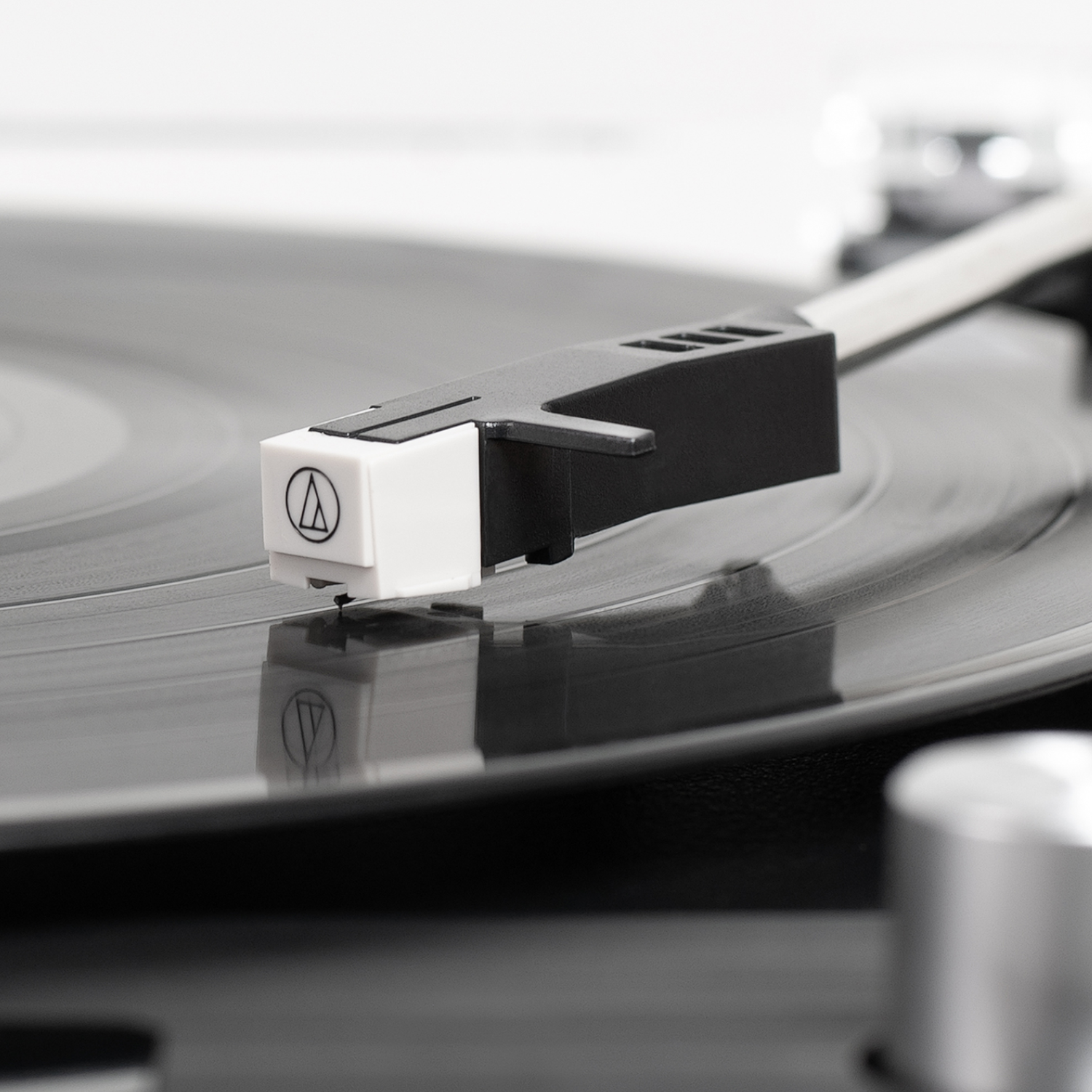 Primo piano di un ago di un giradischi su un disco in vinile. Bianco e nero, con logo.