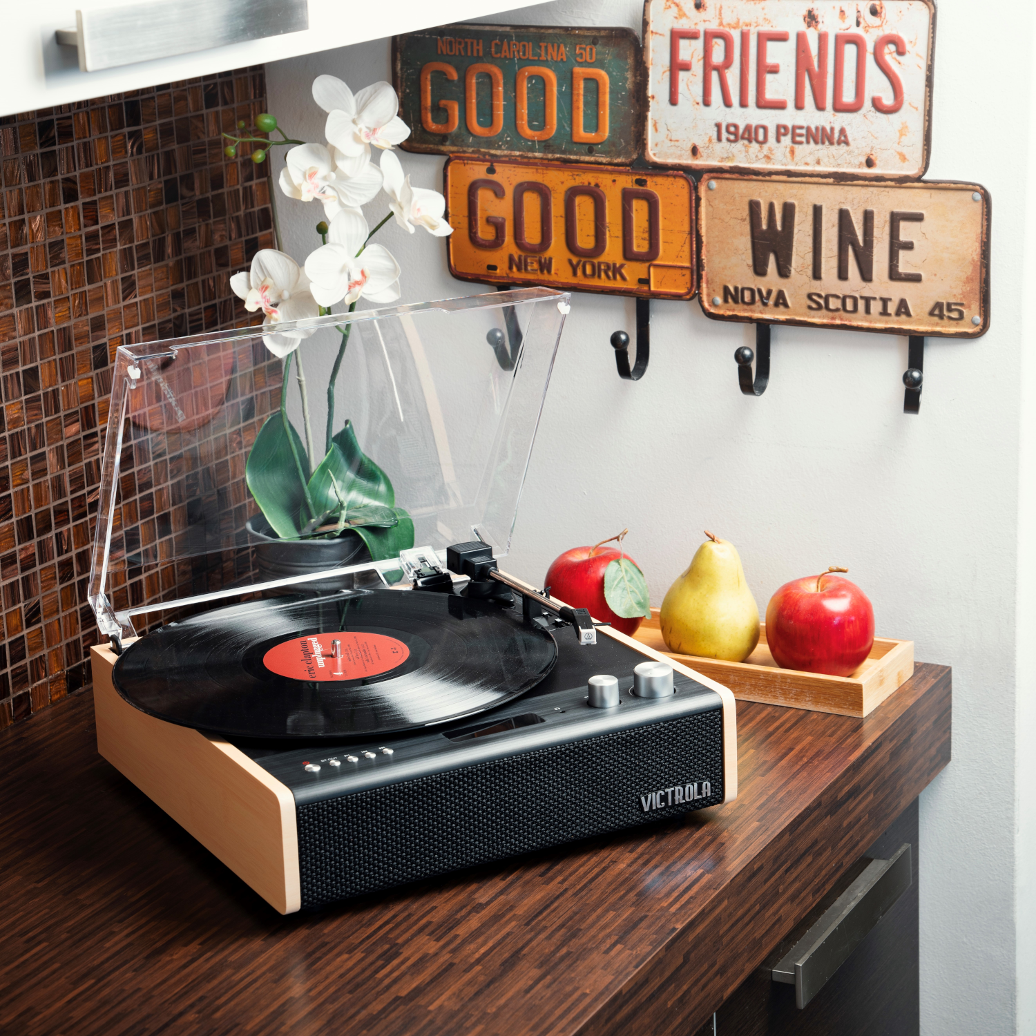 Un giradischi con un disco, con mele, pere e piatti decorativi in un ambiente cucina.