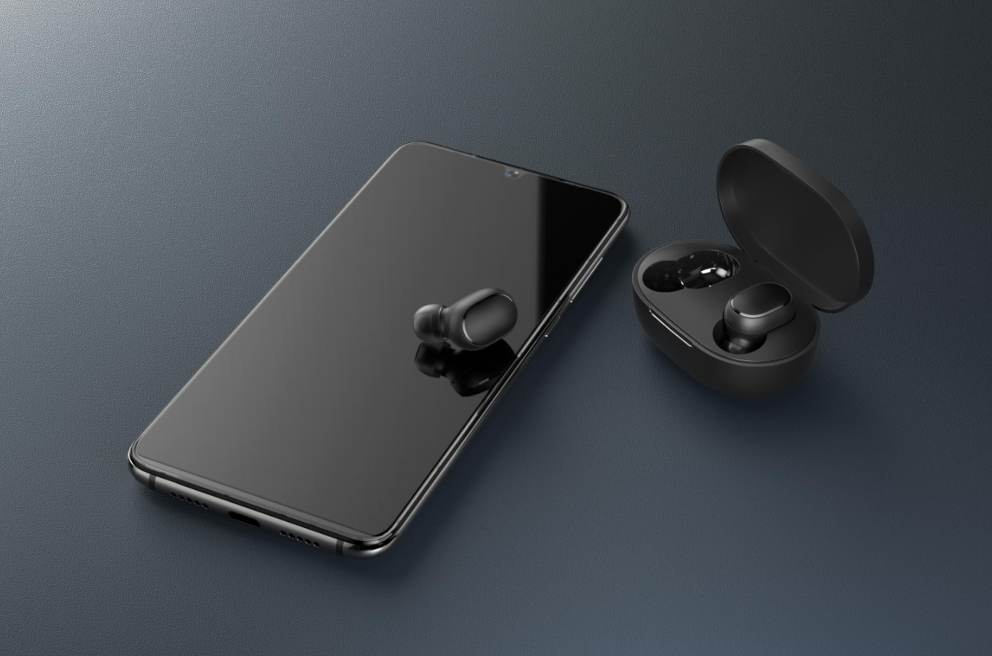 Czarny smartfon ze słuchawkami. Słuchawki w etui i jedna z przodu. Ciemne tło.