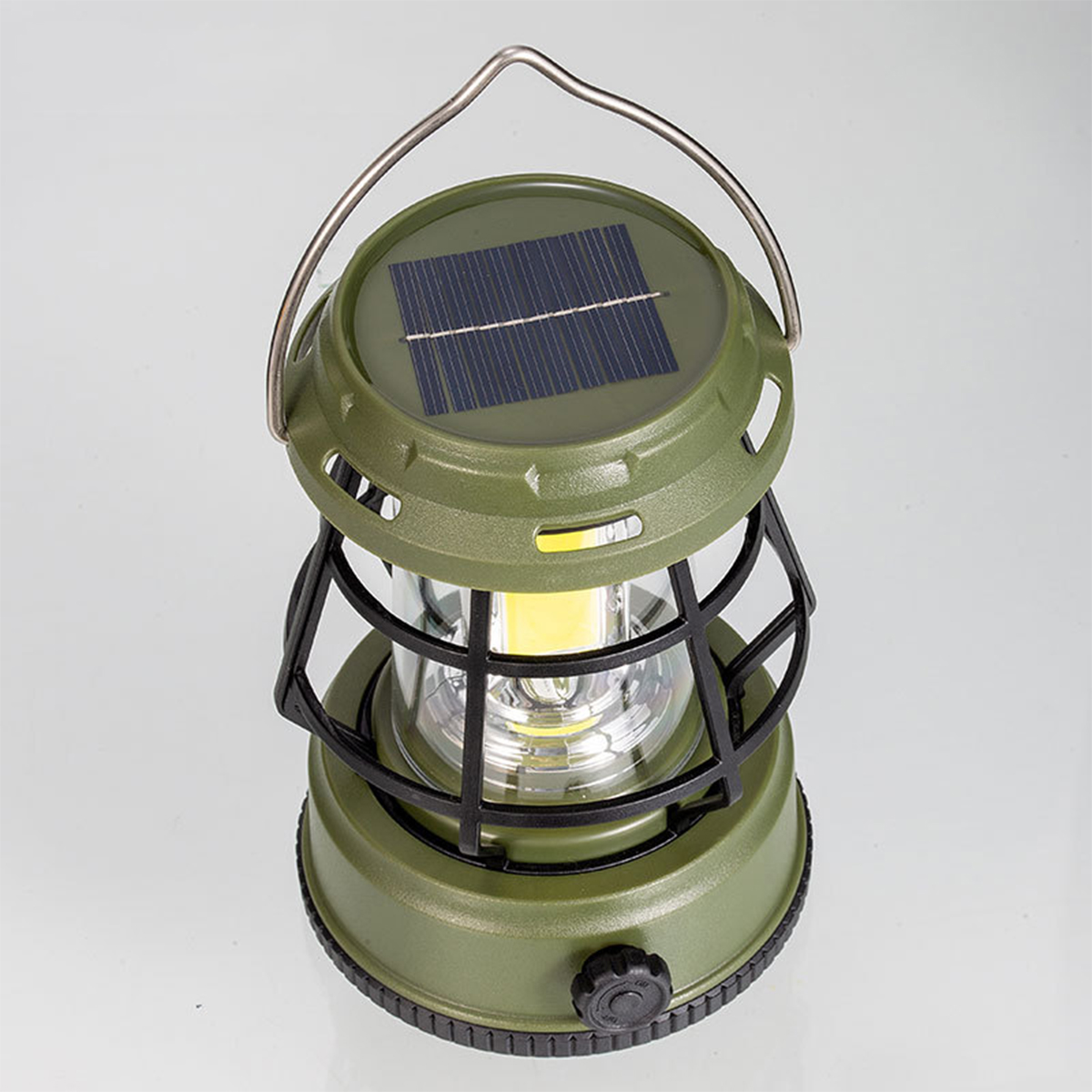 Grüne Campinglaterne mit Solarpanel, schwarzem Käfig und Henkel auf weißem Untergrund.