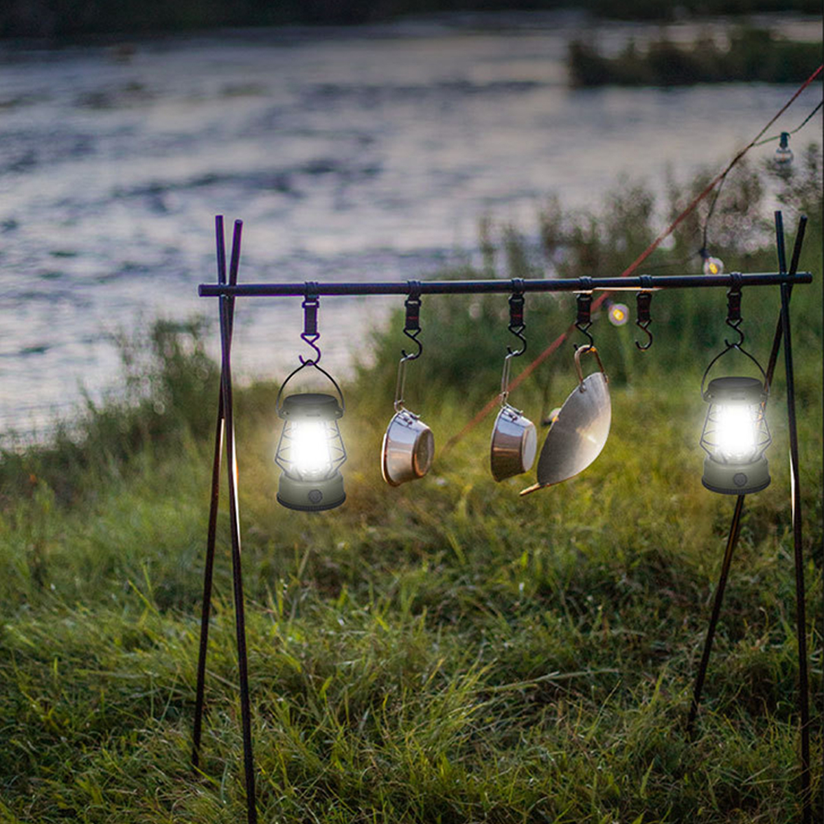 Camping-Szene: Laternen und Kochtöpfe hängen über einem Bach mit Gras im Vordergrund.
