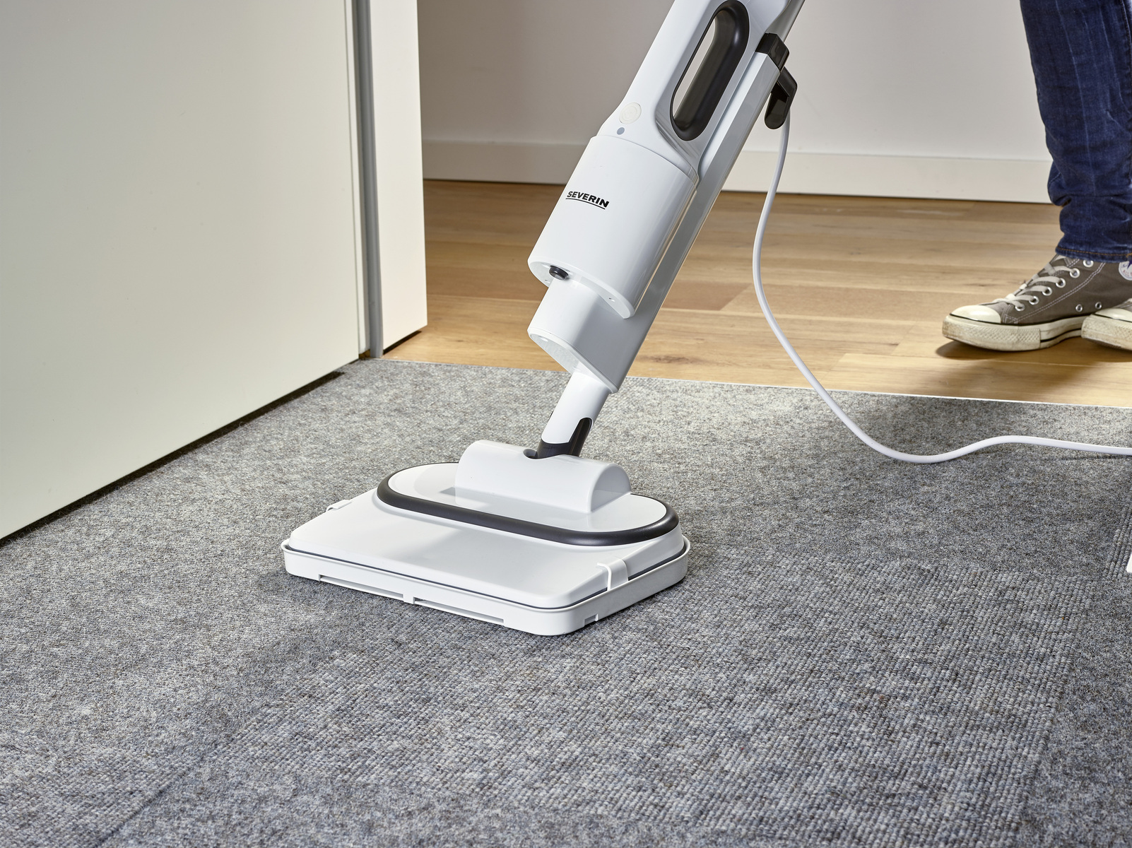 Una persona che pulisce un tappeto con un pulitore a vapore bianco.