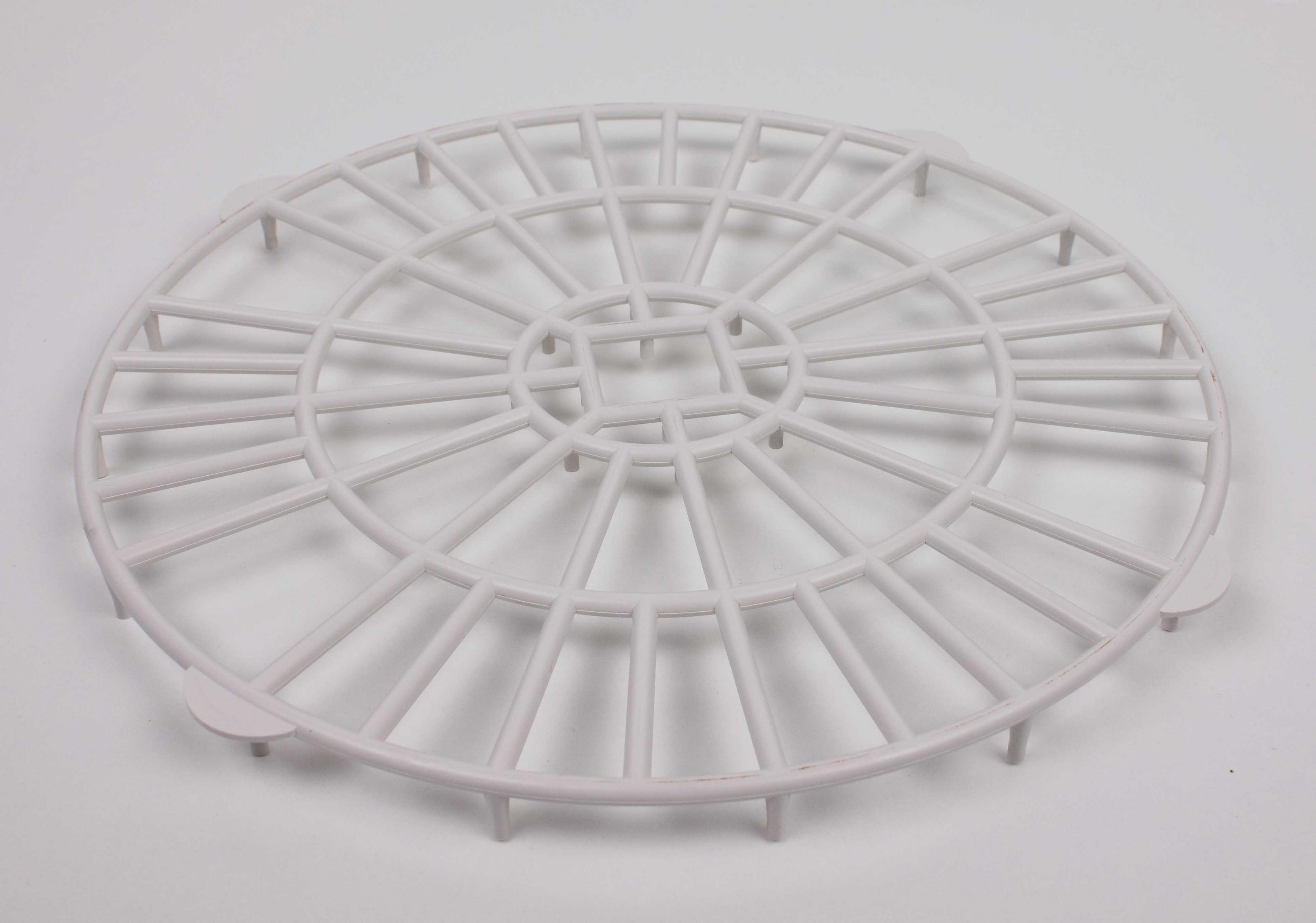 Una griglia rotonda di plastica bianca. Ha molte linee radiali e alcuni supporti rotondi.
