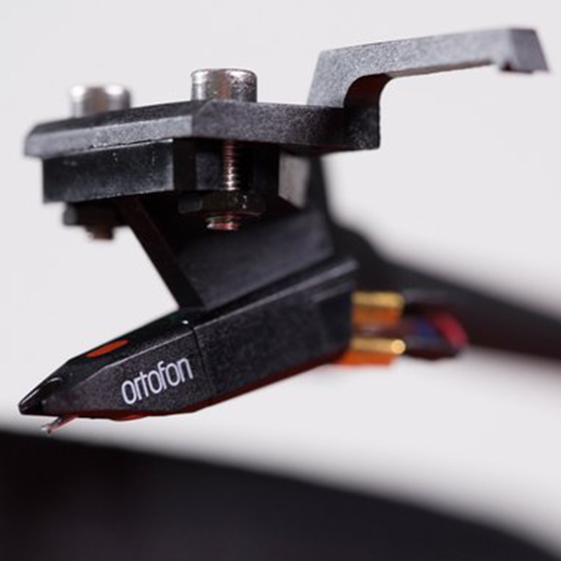 Close-up van een zwarte Ortofon-cartridge met een rode stylus op een witte achtergrond.