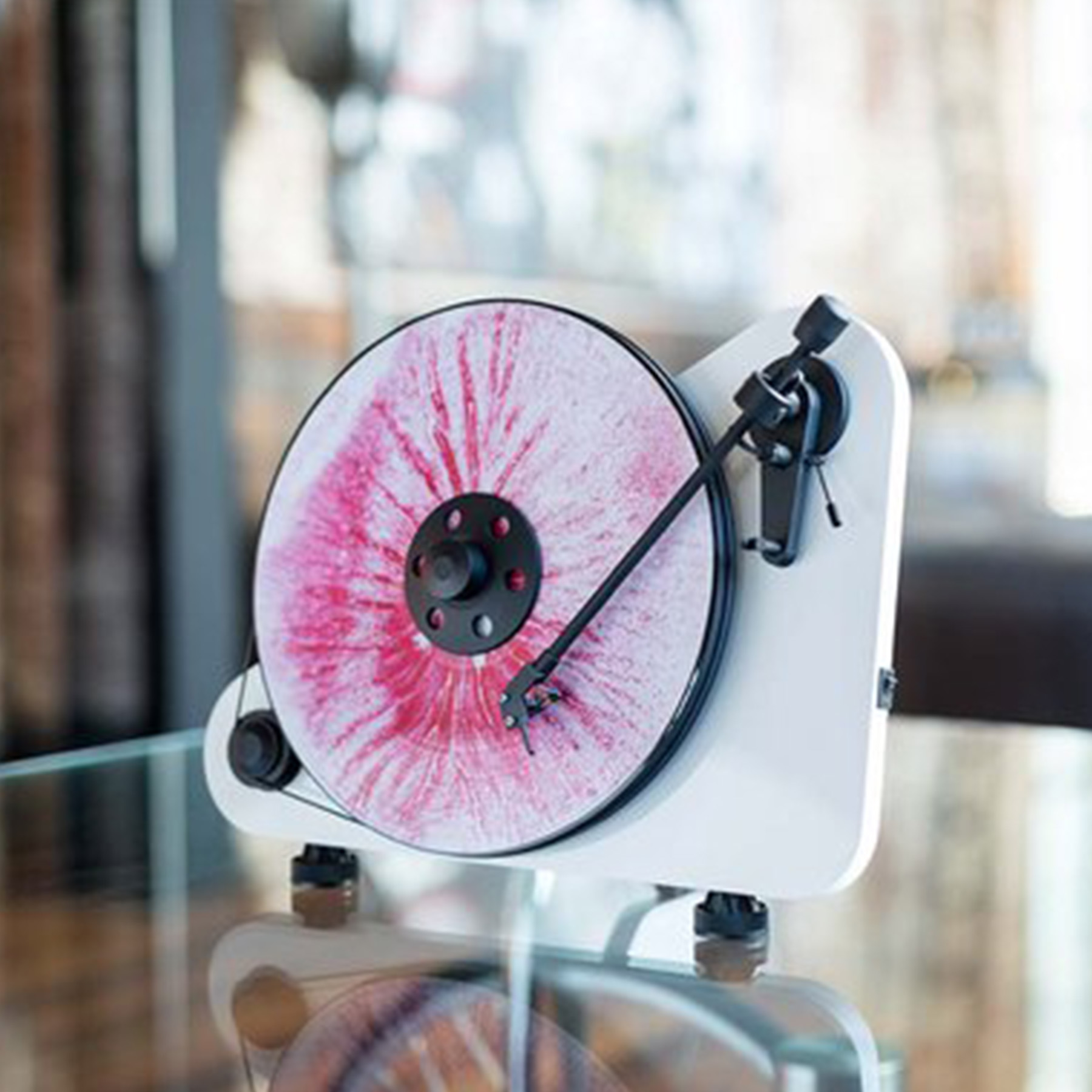 Gramofon z czerwoną i białą płytą winylową. Biała podstawa, czarne ramię i szklana powierzchnia.