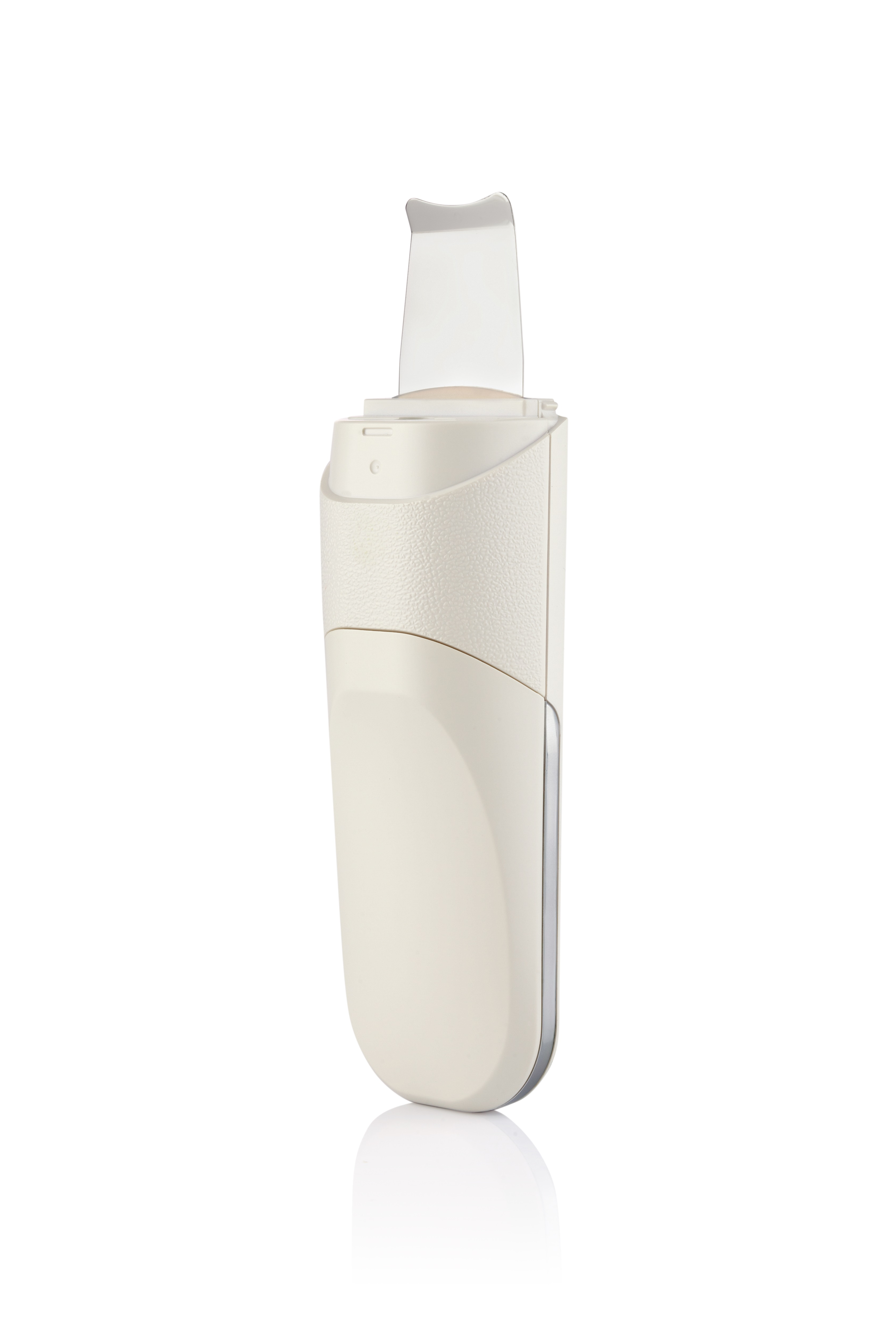 Una herramienta de limpieza facial blanquecina con una cuchilla plateada, sobre blanco. Superficie reflectante debajo.