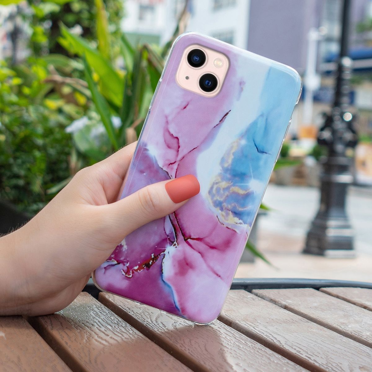 Hand hält Telefon mit bunter Hülle. Hülle hat rosa und blaue Muster.