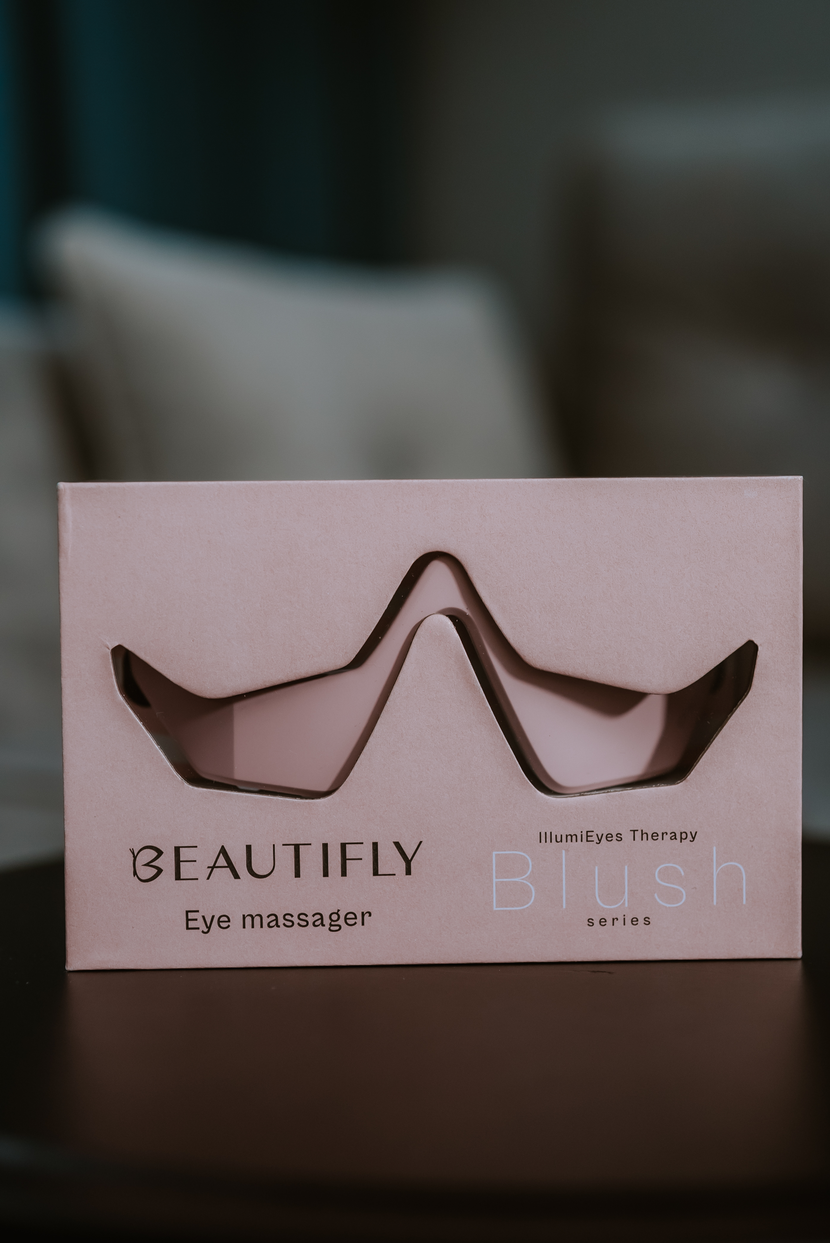 Opakowanie masażera do oczu z napisem 'BEAUTIFLY' i 'Blush series' na ciemnobrązowej powierzchni.