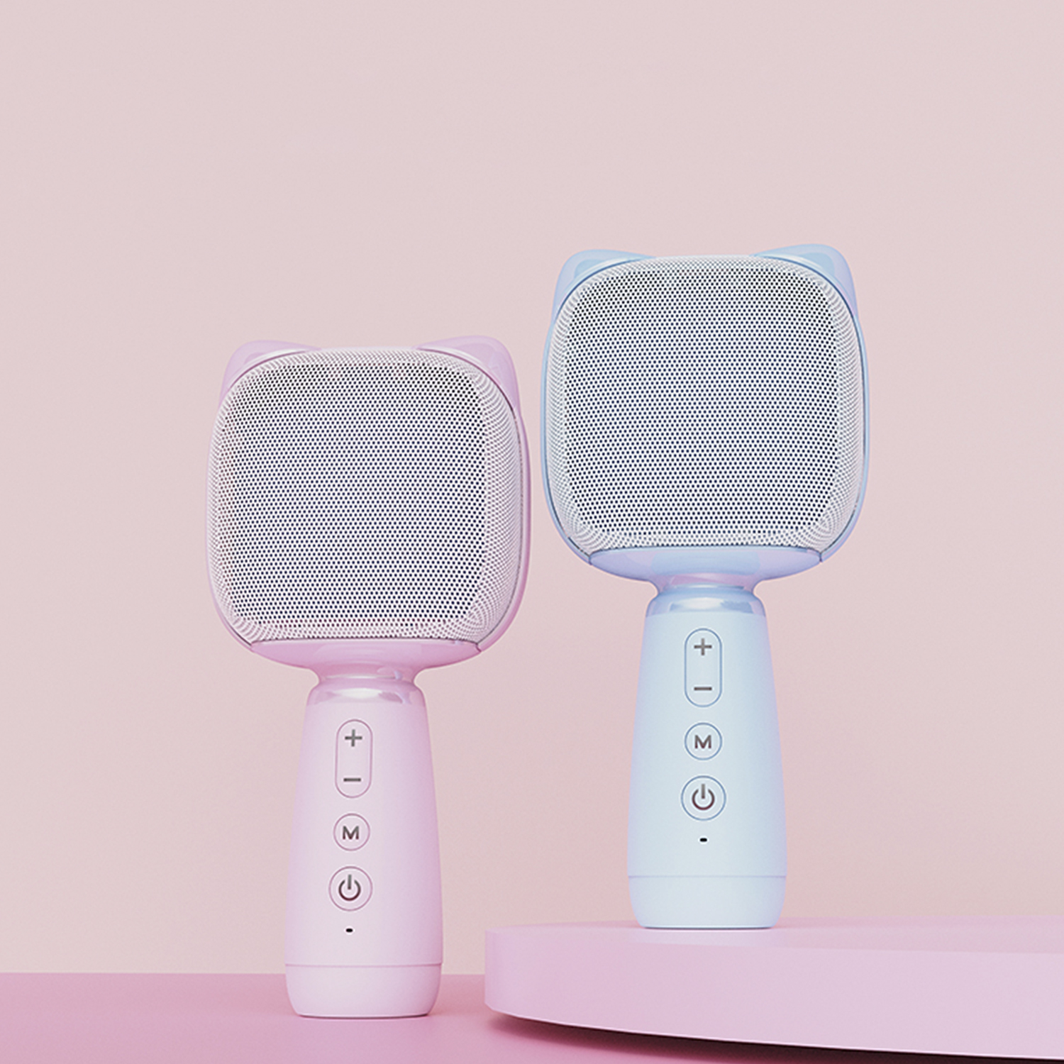 Due microfoni karaoke a forma di gatto, uno rosa e uno blu, su una superficie rosa.
