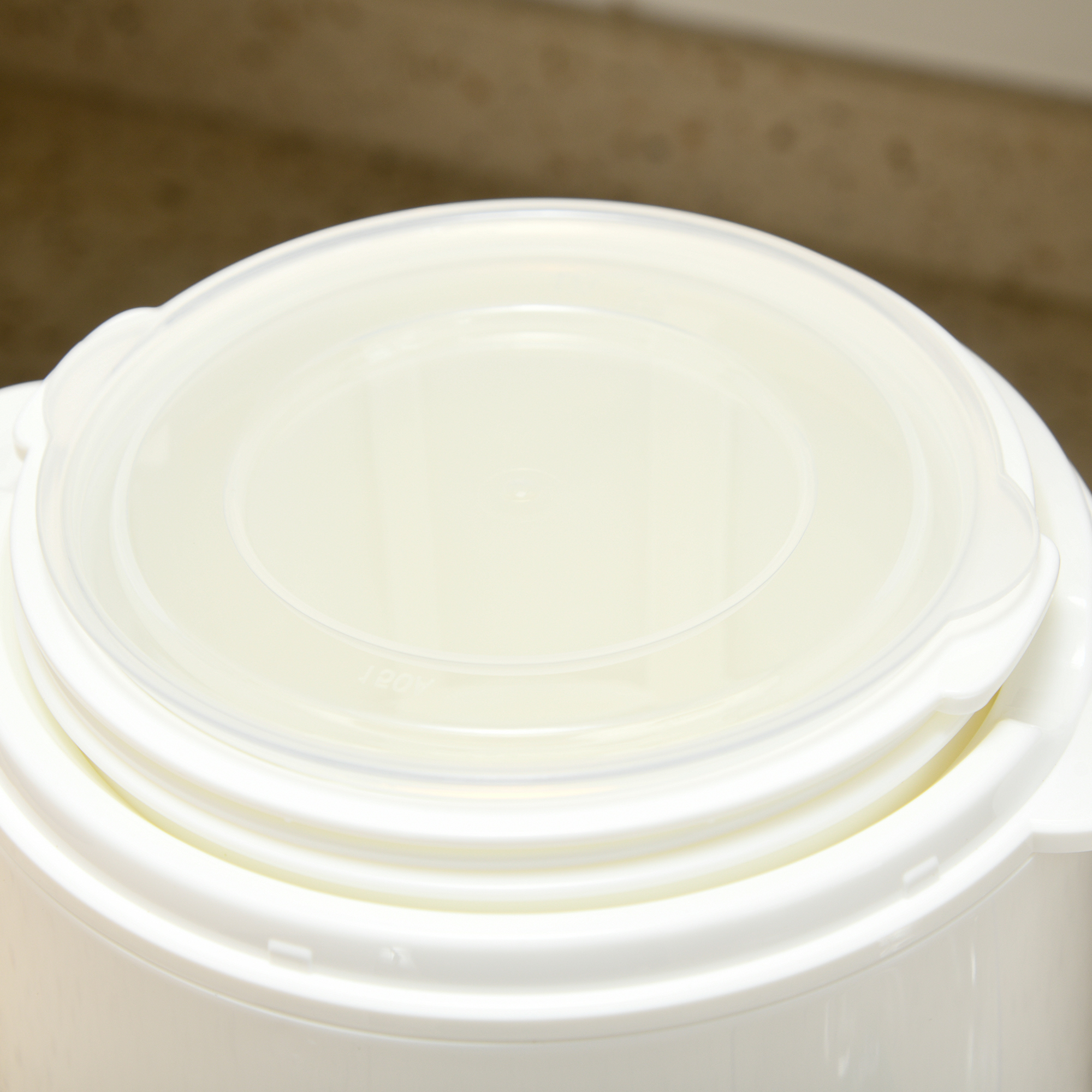 Primer plano de un recipiente blanco con tapa sobre una superficie de madera. La tapa es transparente.