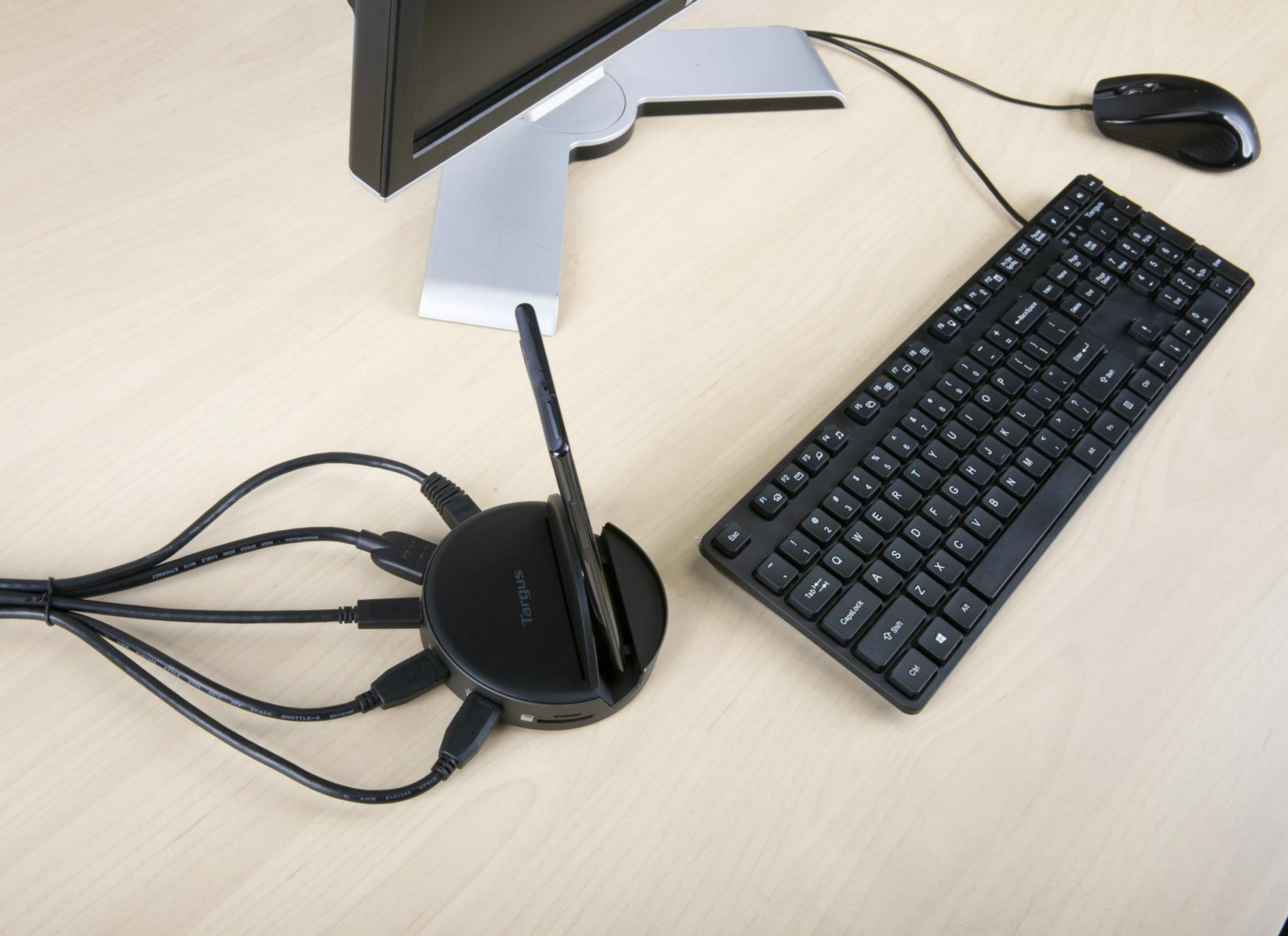 Configurazione scrivania con monitor, tastiera, mouse e un hub nero con cavi collegati.