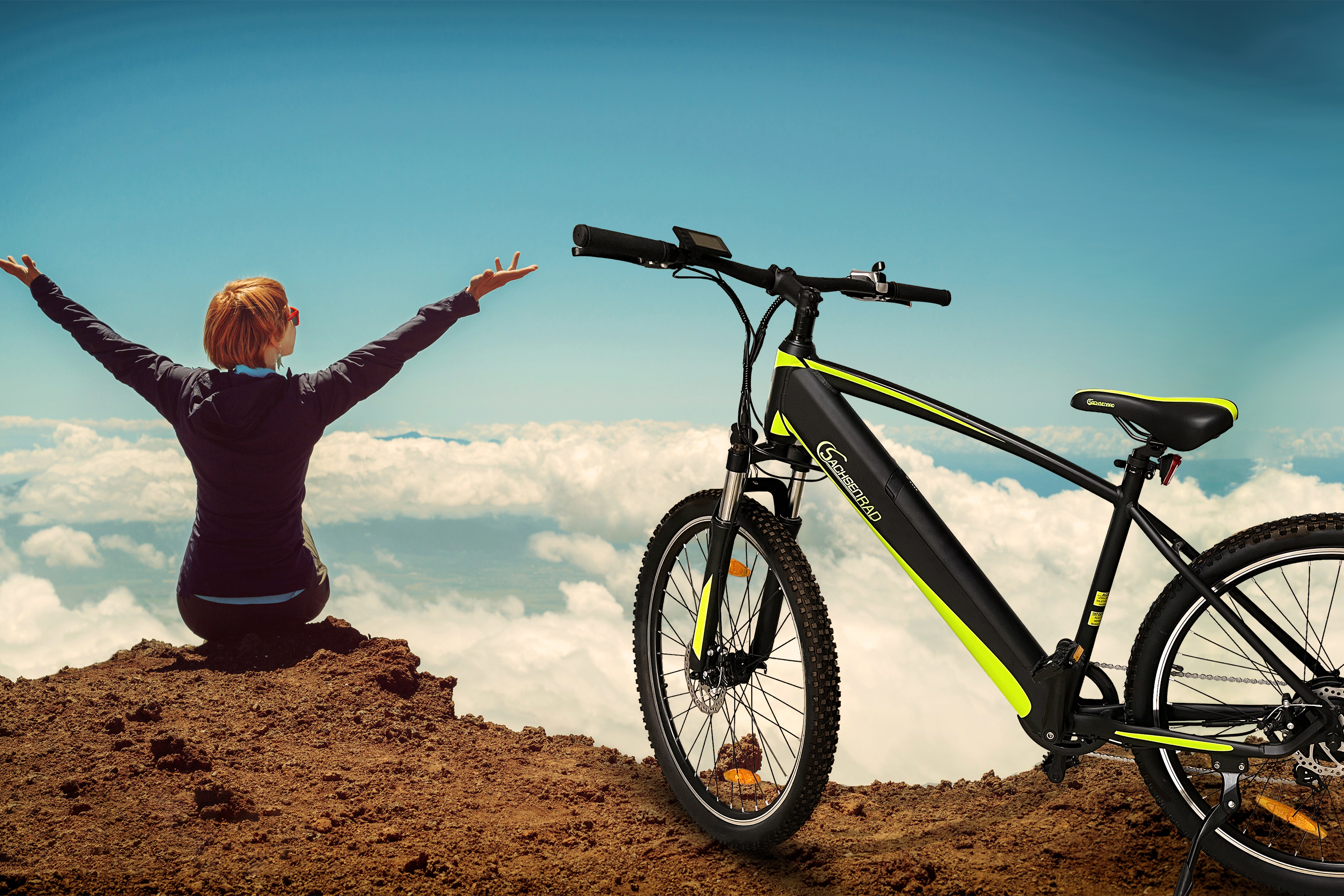 Eine Person steht auf einem Berg neben einem schwarz-gelben Elektrofahrrad. Himmelshintergrund.
