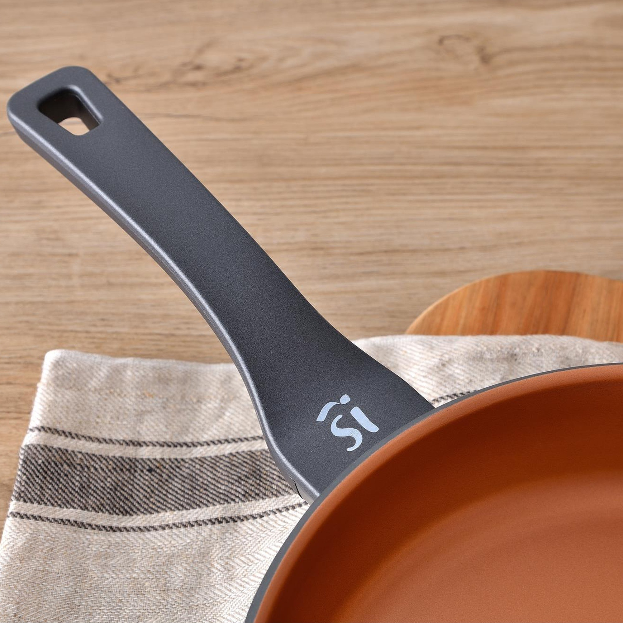 Primer plano de sartén con mango gris oscuro y tabla de cortar de madera.