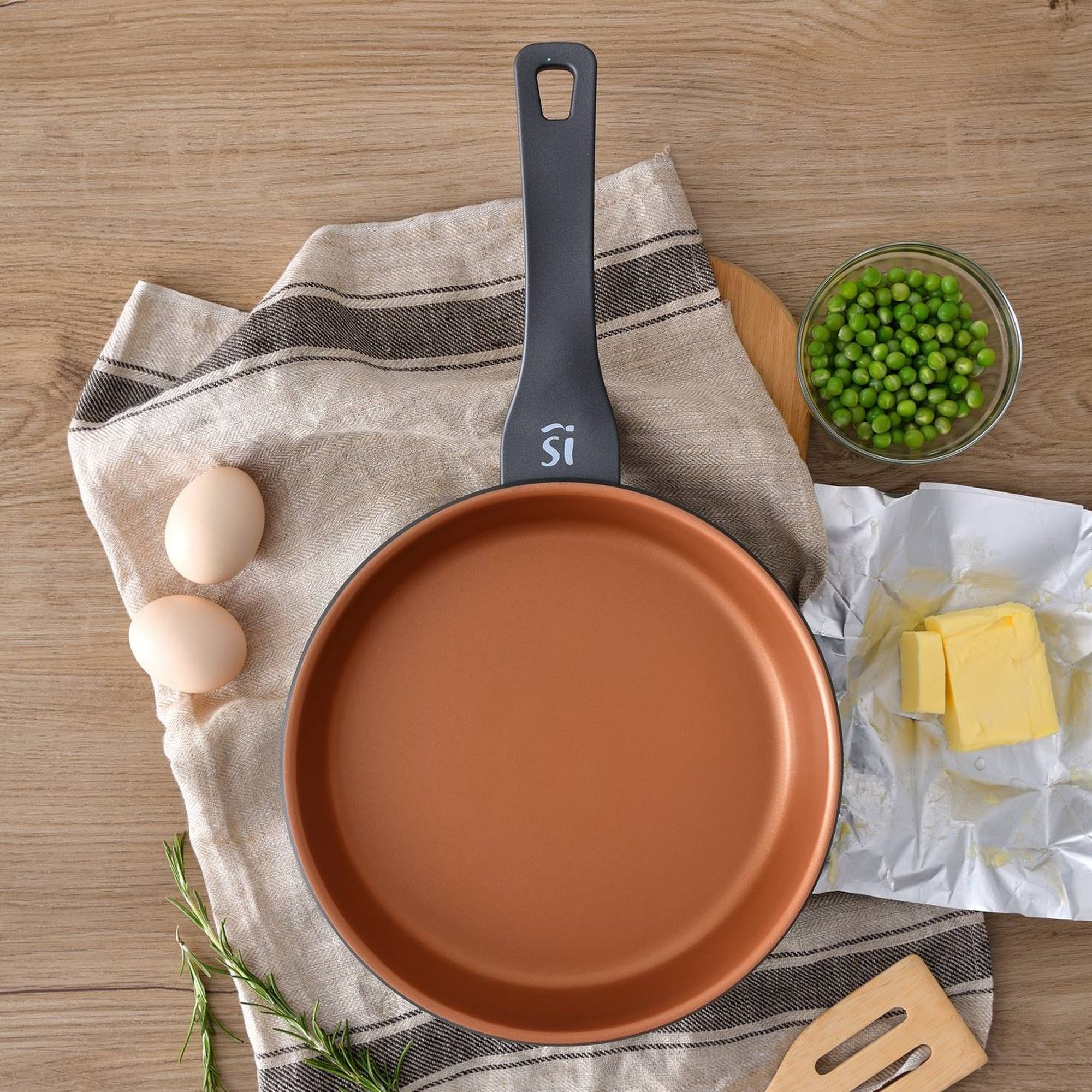 Sartén con ingredientes: huevos, mantequilla, guisantes.