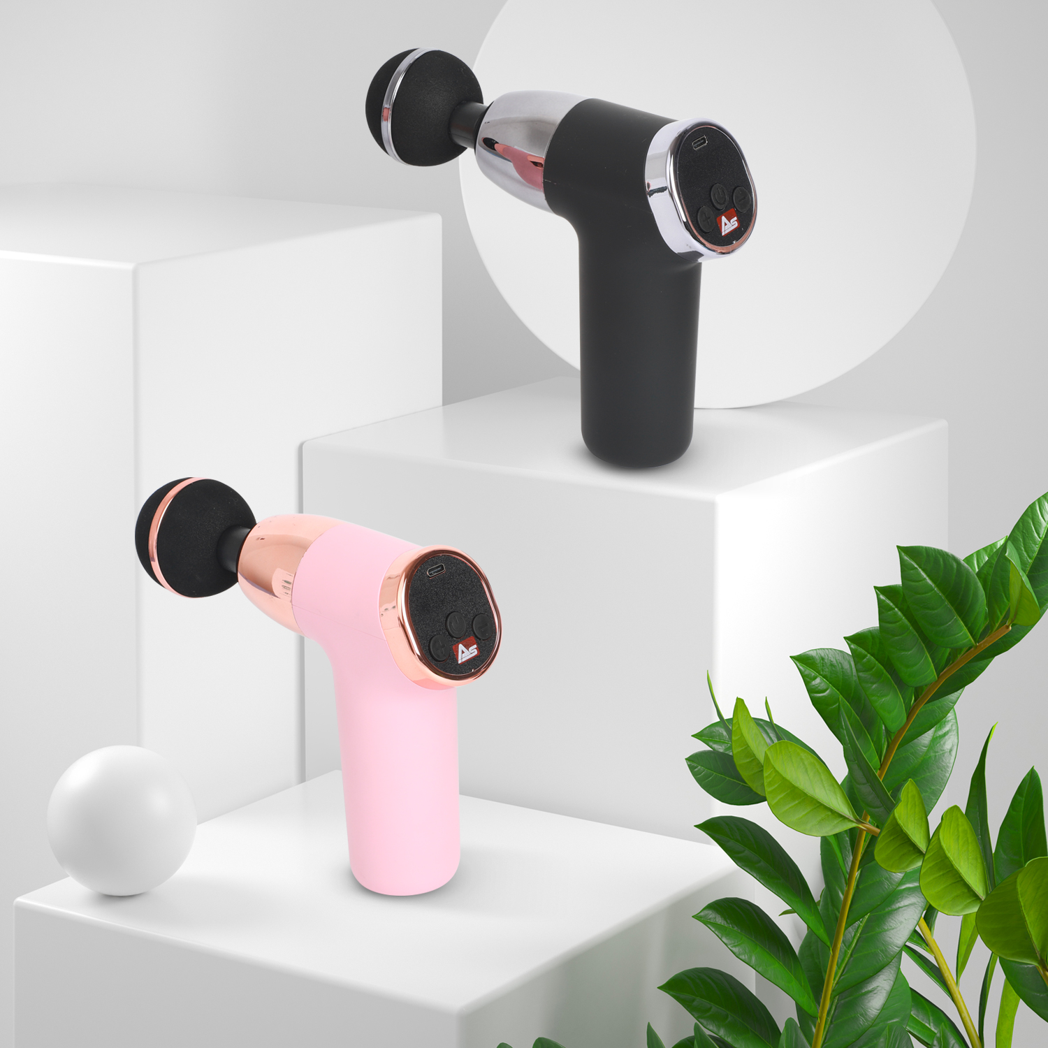 Zwei Massagepistolen, schwarz und rosa, auf weißen Blöcken mit Pflanzen.