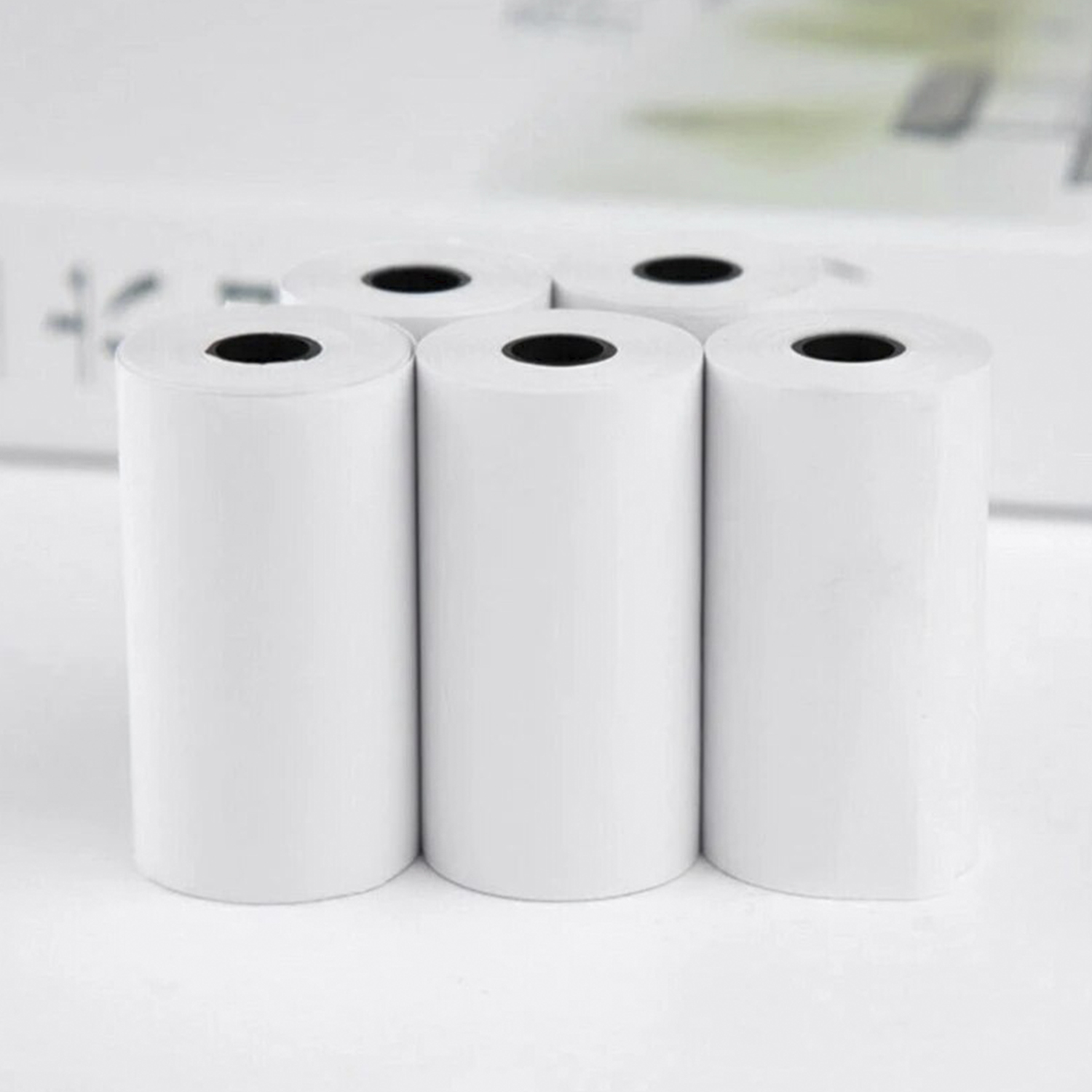 Cinco rollos de papel blanco en disposición vertical, contra un fondo borroso.