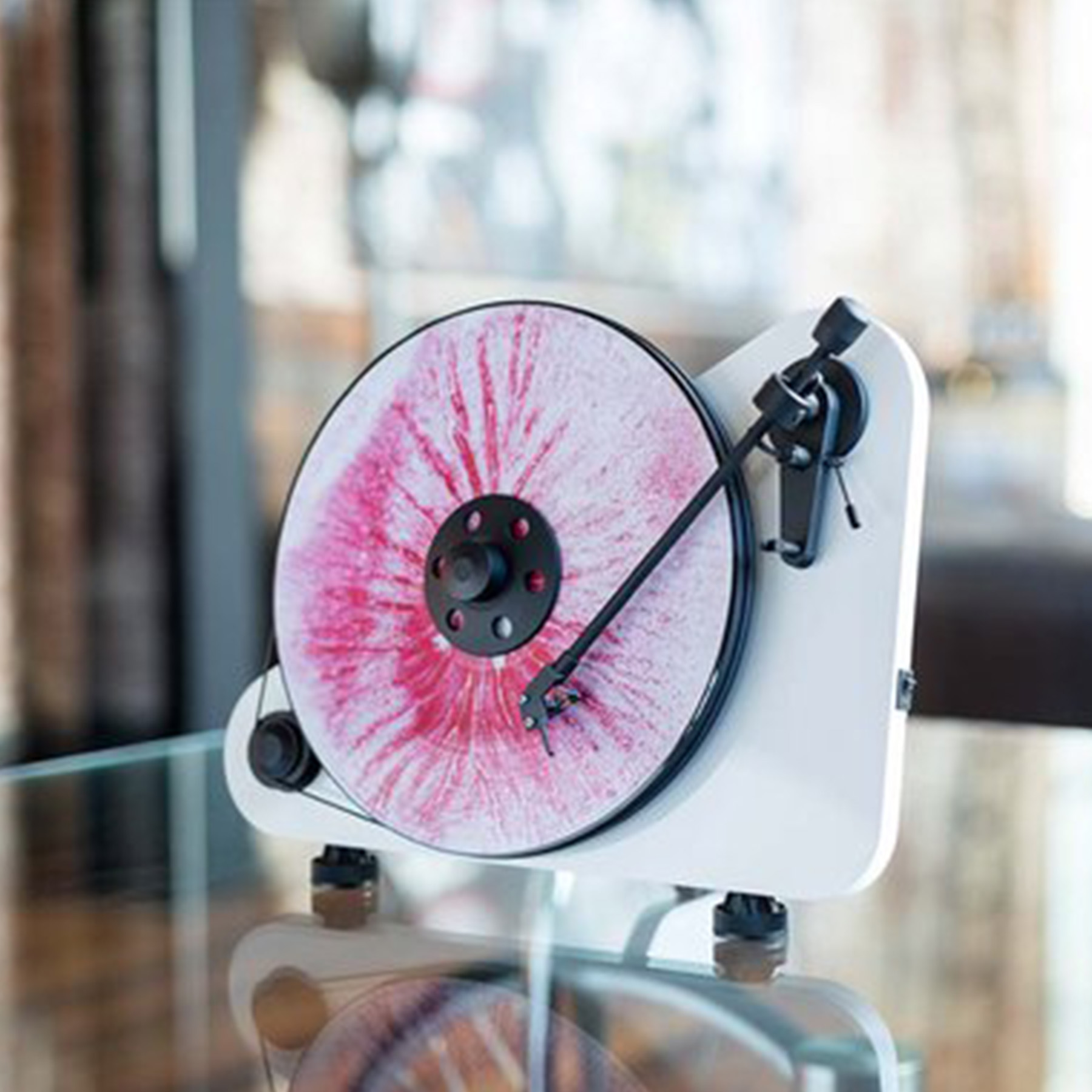 A white record player with a colorful record playing on it, set against a blurry background.