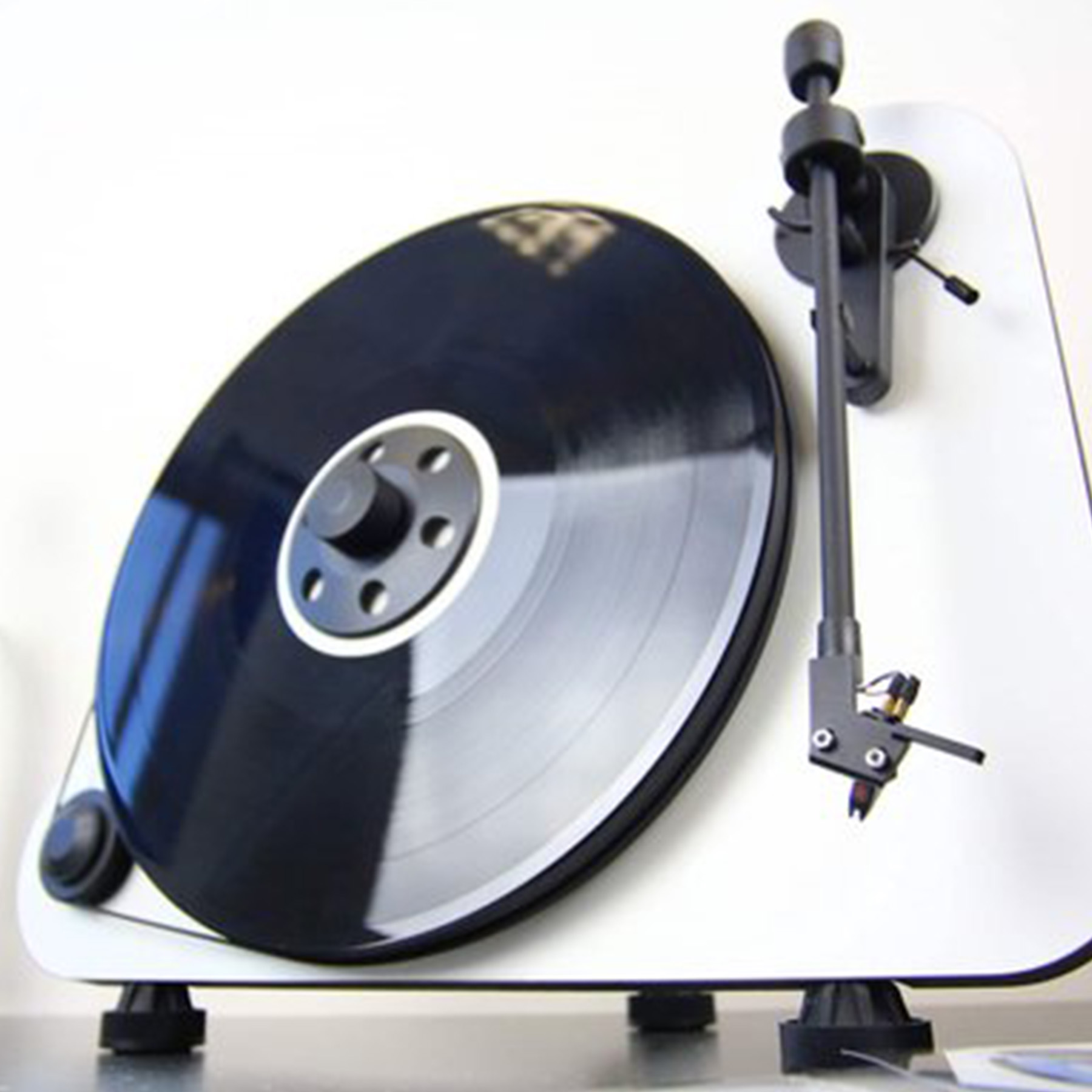 A black vinyl record on a white turntable. The tone arm and base are black.
