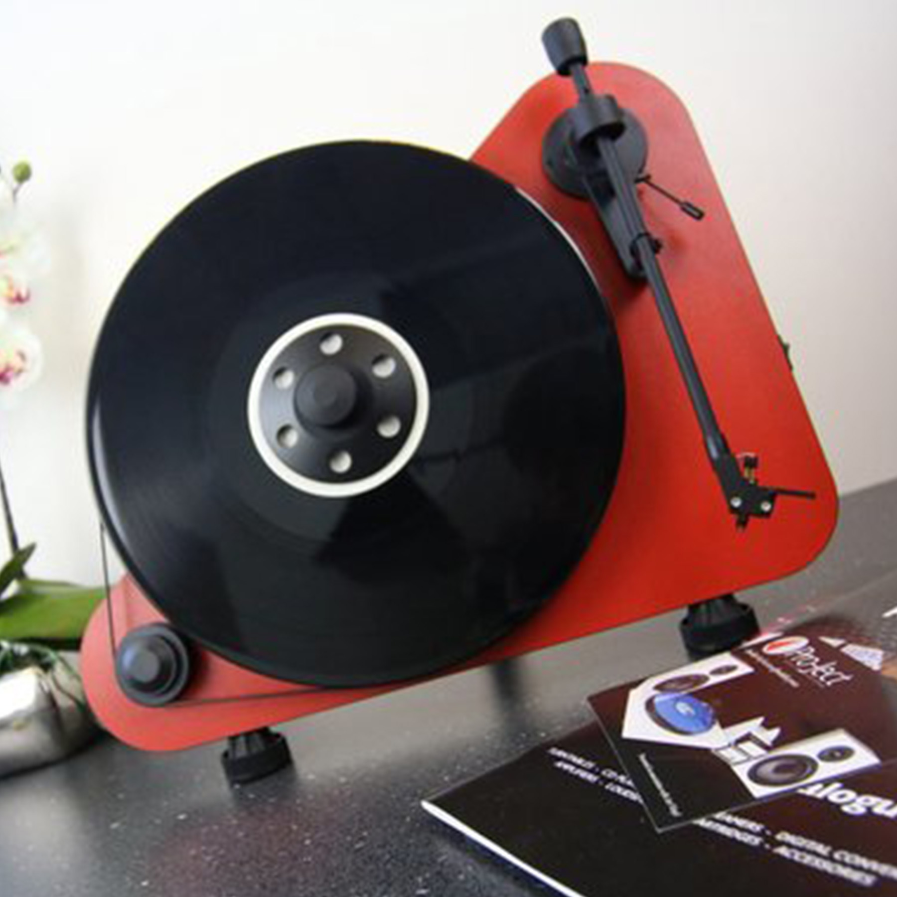 Rode platenspeler met zwarte plaat. Twee brochures op de tafel.