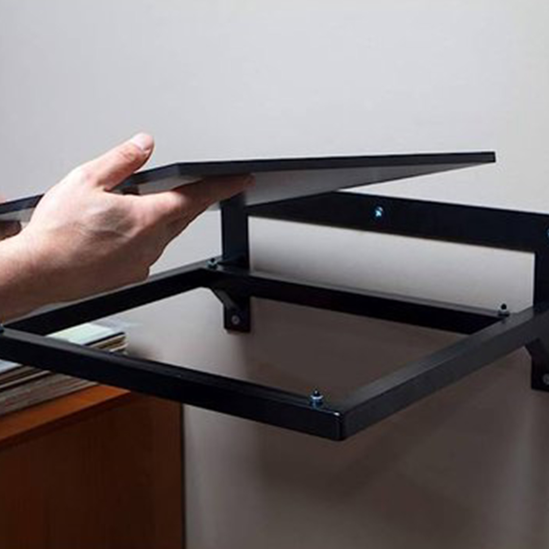 Zwart schap wordt geïnstalleerd. Hand houdt het schap boven het frame.