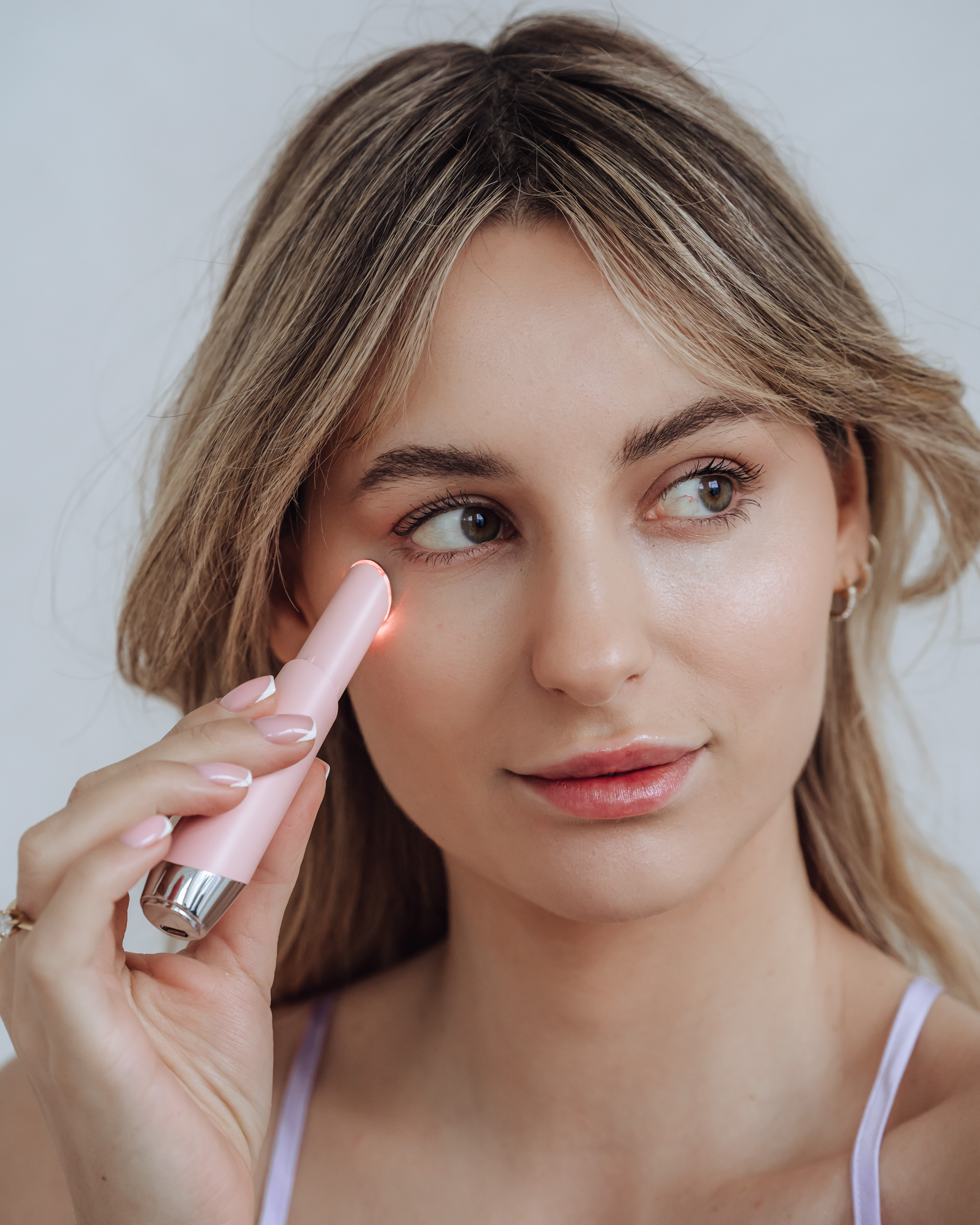 Eine Frau hält ein rosa Gerät in der Nähe ihres Auges, mit sanftem Ausdruck und blonden Haaren.