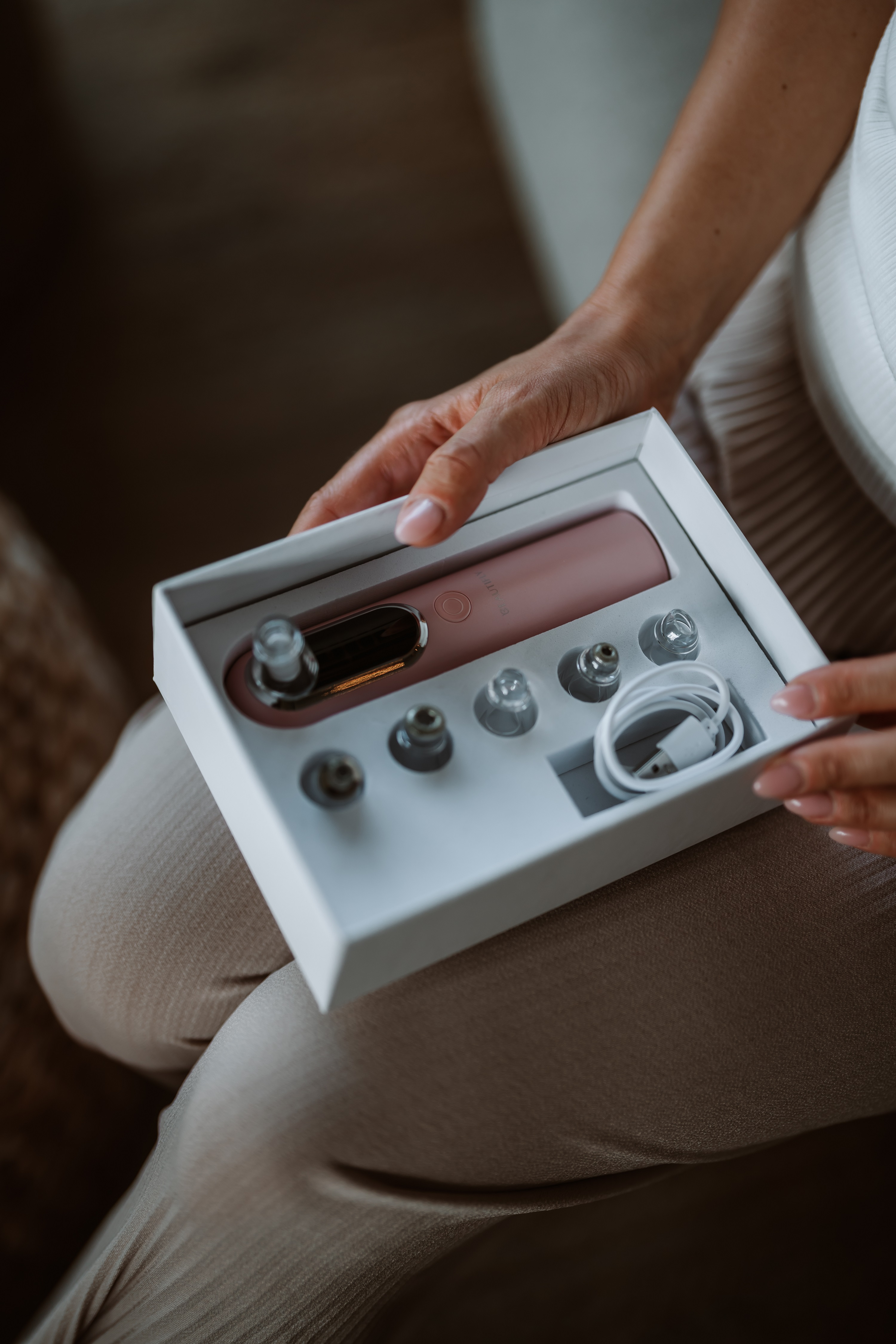 Osoba trzymająca białe pudełko zawierające różowy odkurzacz do porów twarzy i akcesoria.