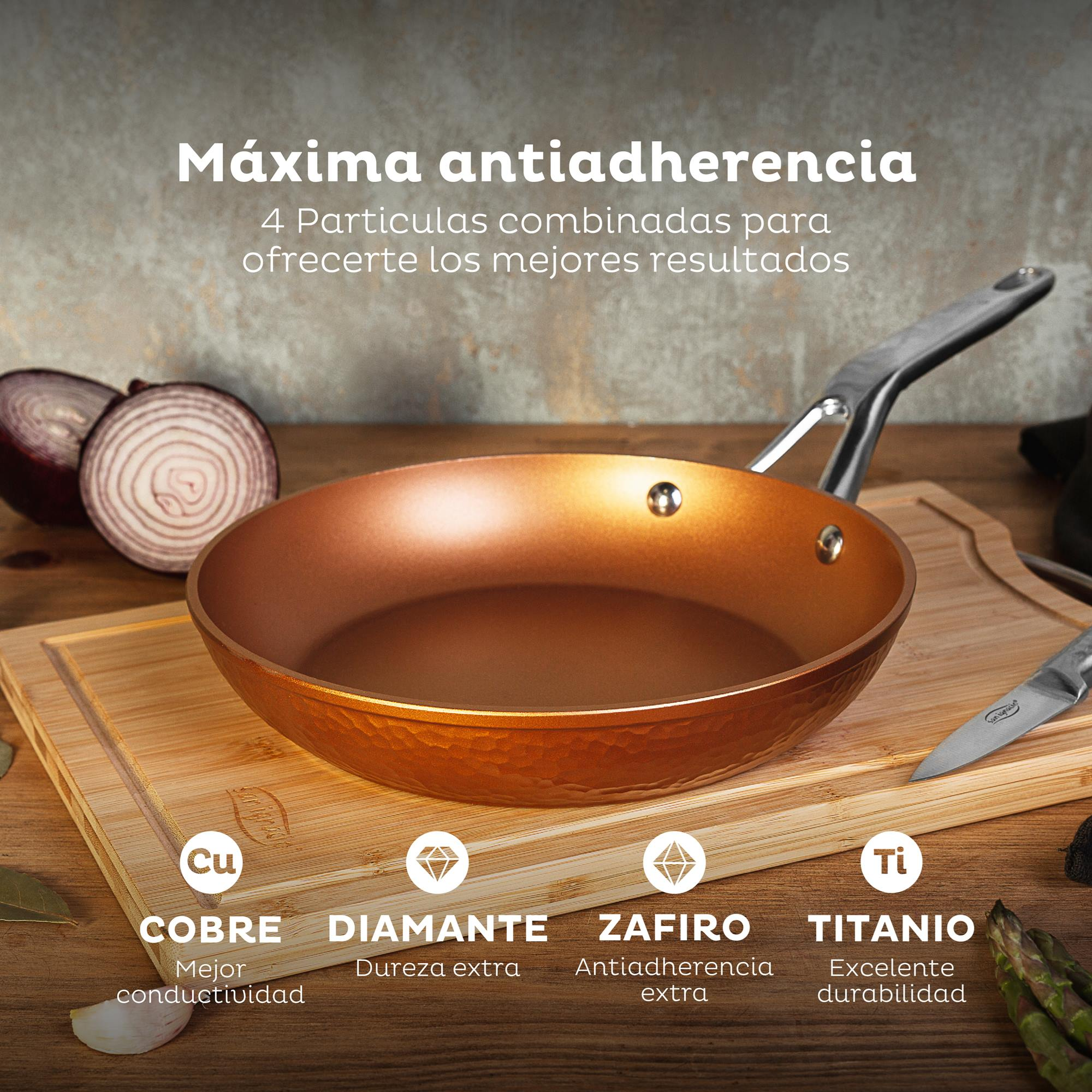 Sartén de cobre sobre tabla de madera con cebollas y espárragos. Texto: Máxima antiadherencia.