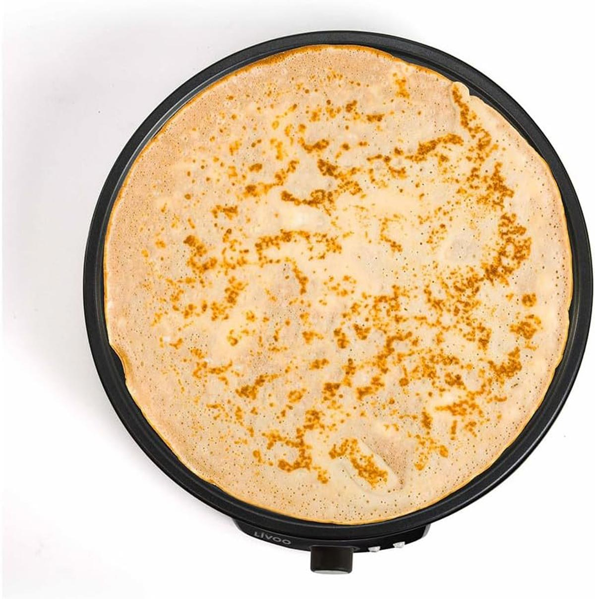 Duży, okrągły naleśnik na czarnej patelni. Jest złocistobrązowy z ciemniejszymi brązowymi plamami i białym tłem.