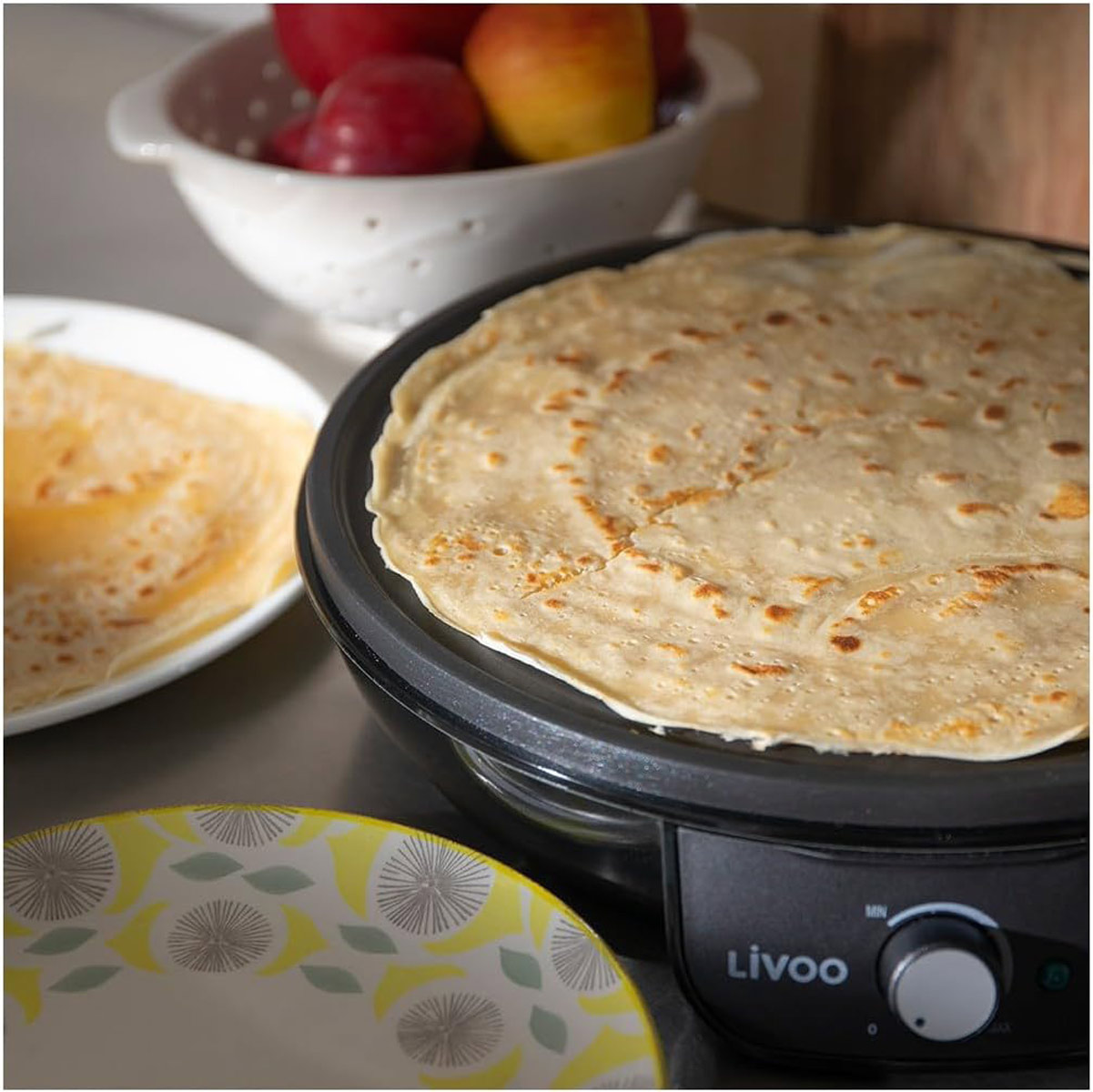 Naleśniki smażone na czarnej patelni, z talerzami i owocami w tle.