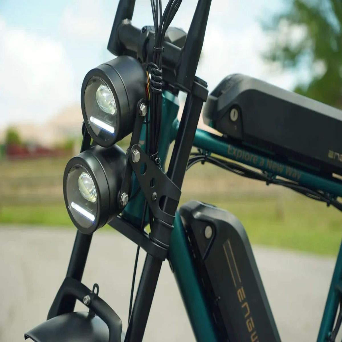 Primo piano della parte anteriore di una e-bike, con doppi fari, manubrio e batteria. Colore verde.