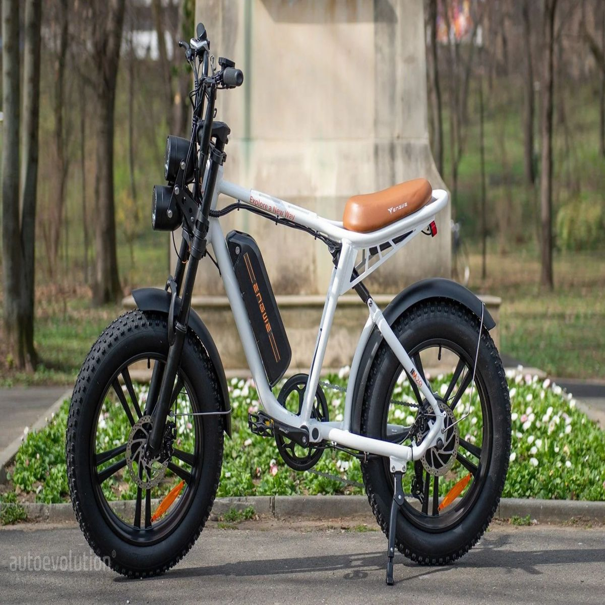 Una bici elettrica con pneumatici larghi, telaio grigio chiaro e sella marrone. La scena è all'aperto.