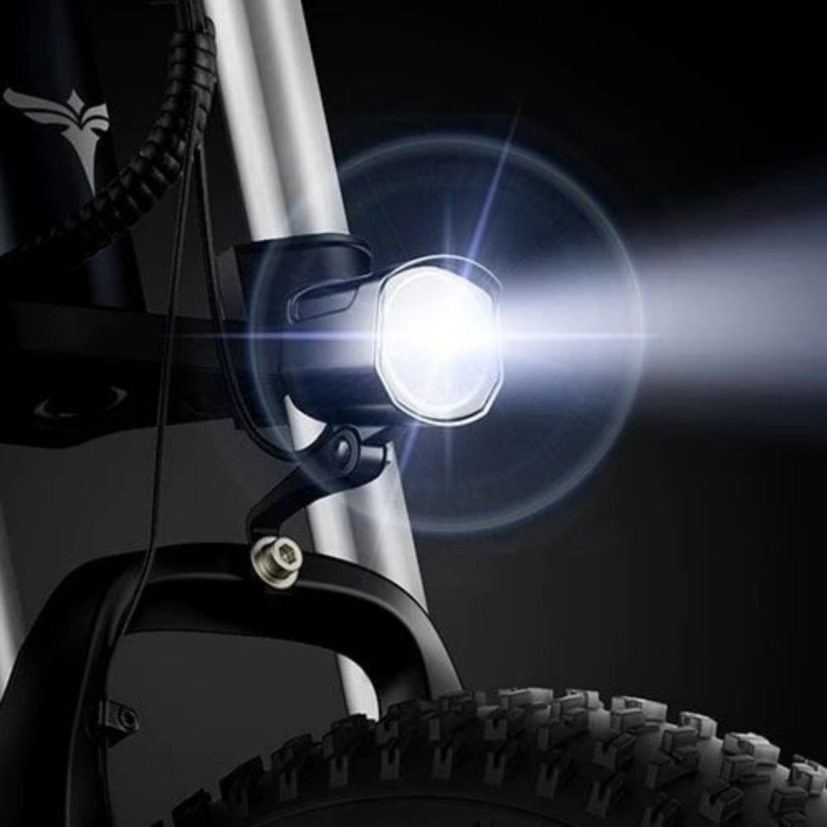 Faro della bicicletta che brilla, con un fascio visibile. Lo pneumatico anteriore è visibile. Sfondo scuro.