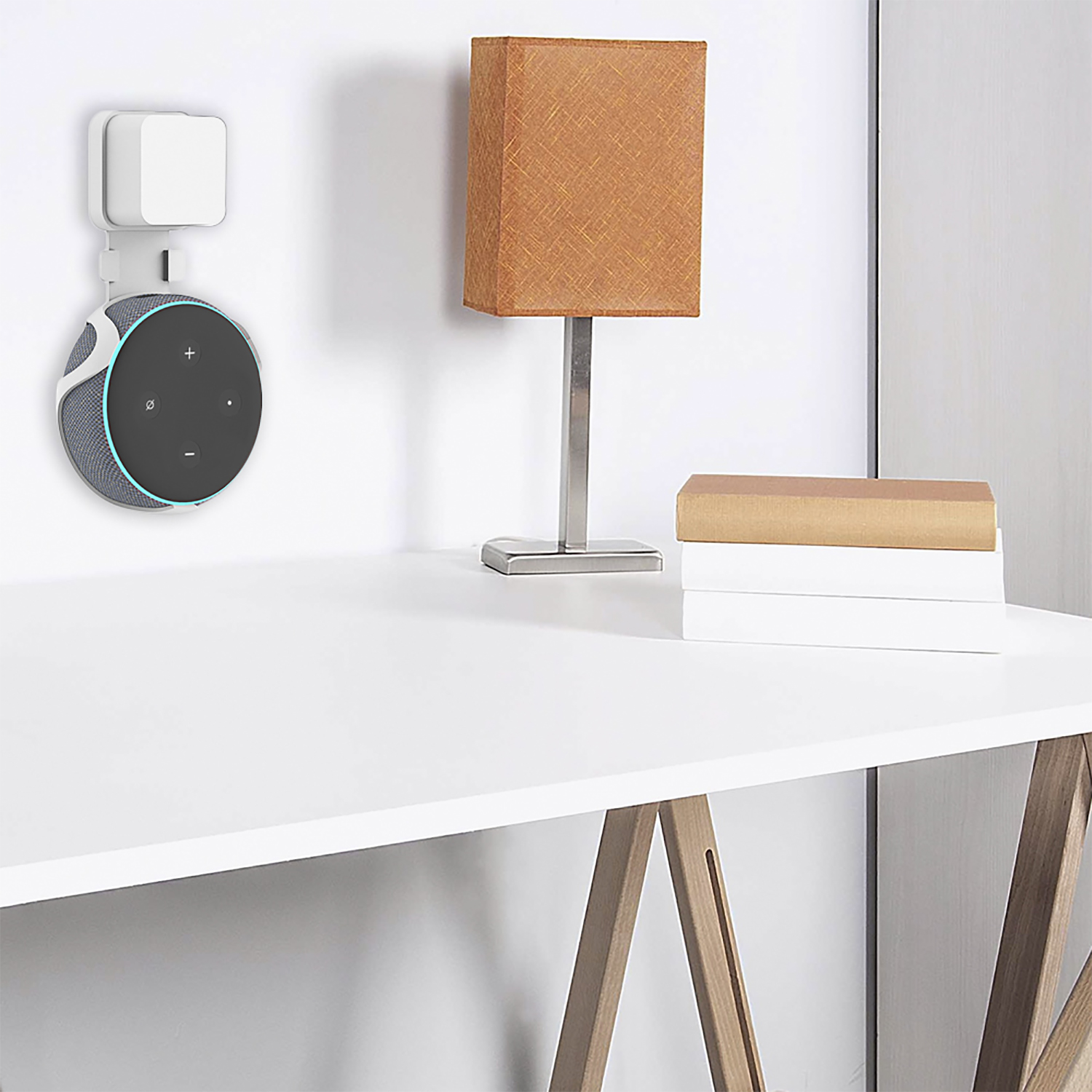Un Echo Dot attaccato a un supporto a parete. Una lampada e libri su una scrivania bianca.
