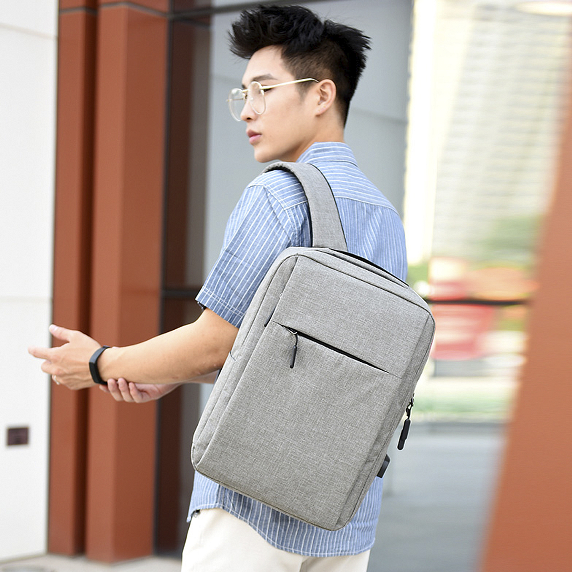 Uomo con una borsa a tracolla grigia, cammina all'aperto. Edifici sullo sfondo.