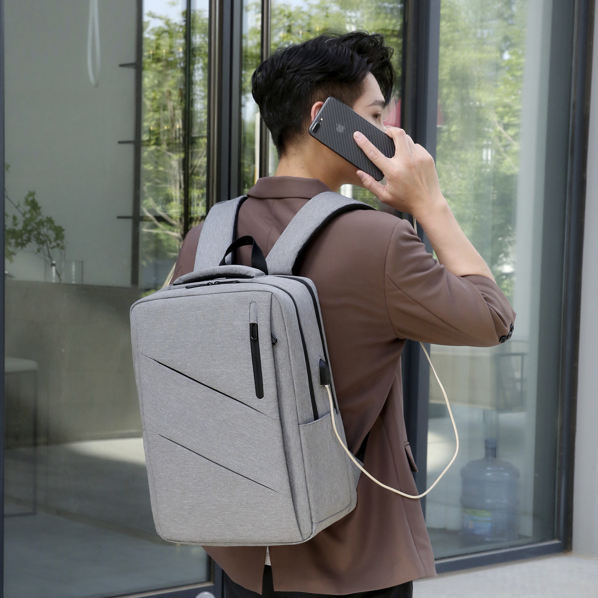 Uomo con zaino che parla al telefono, cavo di ricarica collegato. Sfondo: edificio moderno.