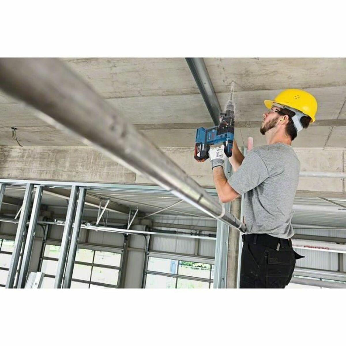 Mann bohrt an Decke. Gelber Helm und Schutzbrille. Baustelle.