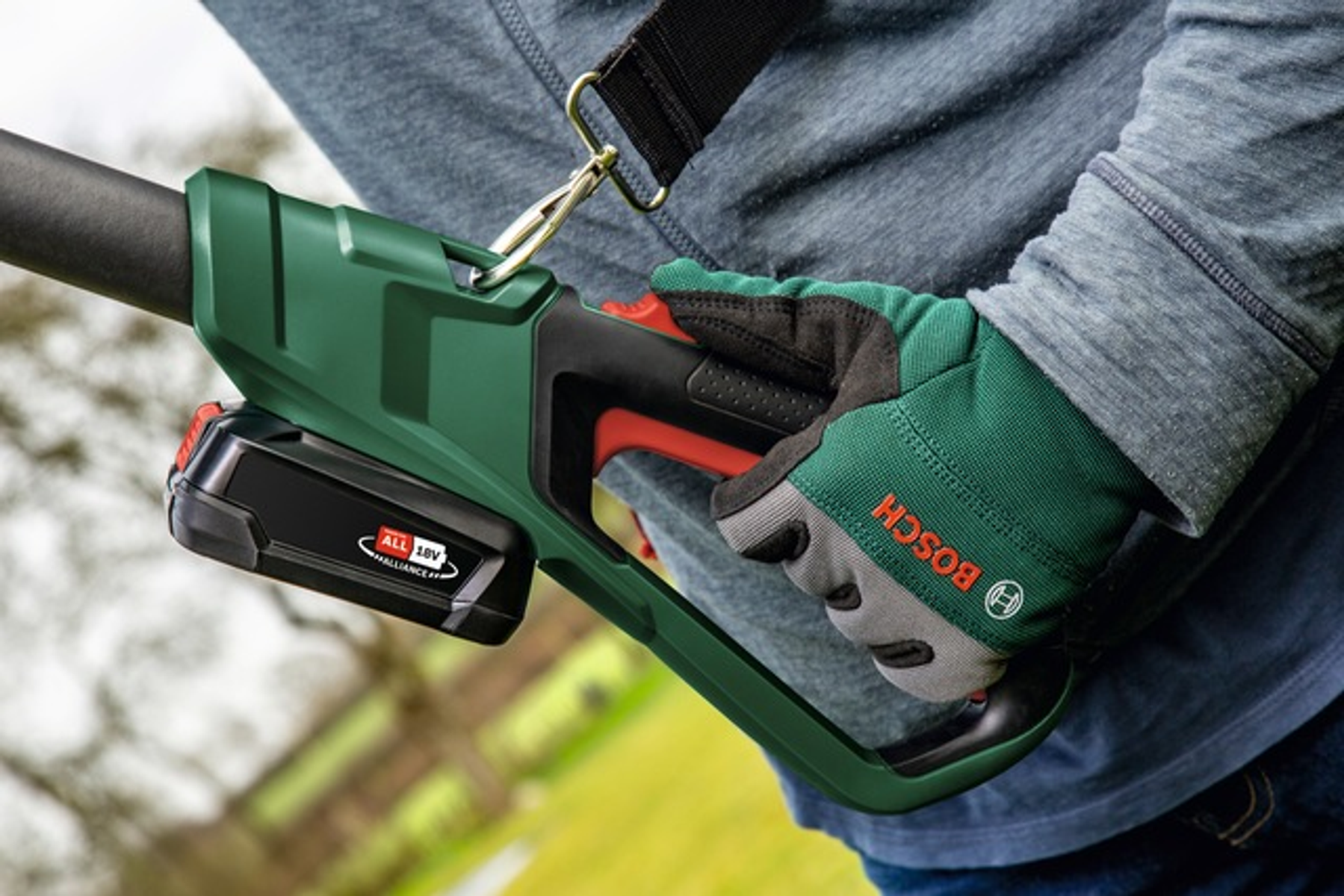 Eine Person hält ein grün-schwarzes Elektrowerkzeug. Das Werkzeug hat einen Akku und das Bosch-Logo.