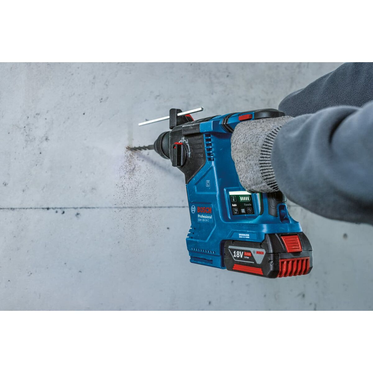 Eine Person benutzt einen blau-schwarzen Bosch-Bohrer an einer Betonwand, Staub vom Bohren sichtbar.
