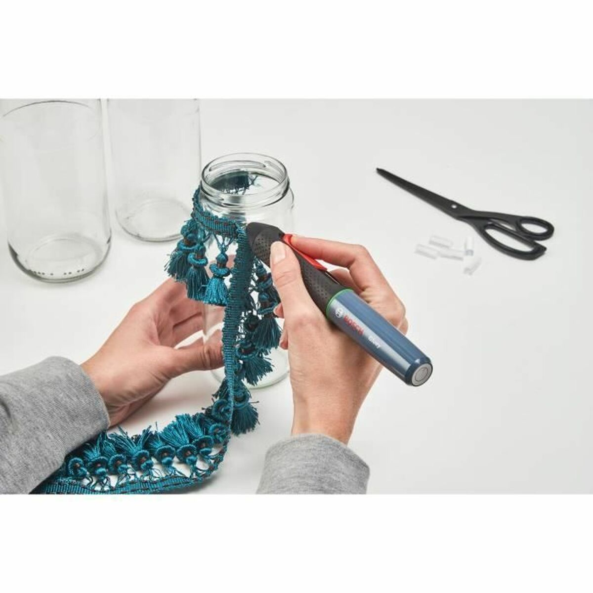 Hände dekorieren ein Glas mit tealfarbenen Quasten, mit Schere und Stift.