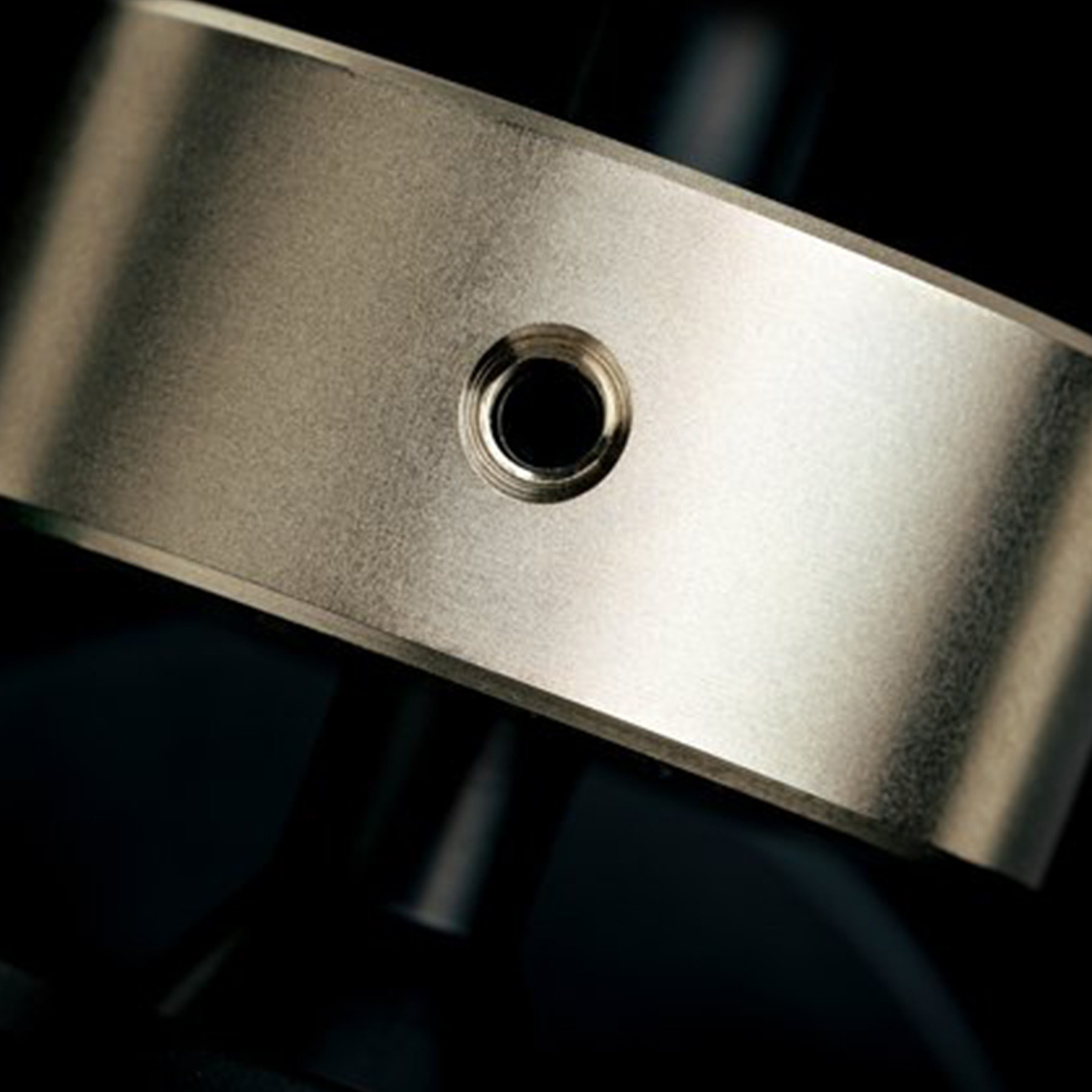 Close-up of a metallic component with a hole, on a blurred, dark background.